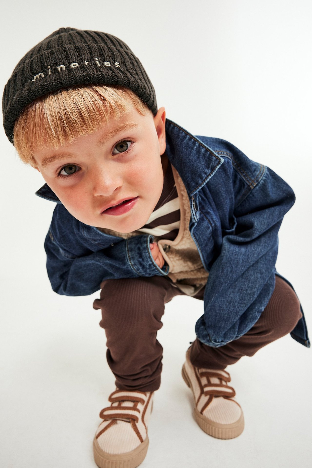 Lapsi tummanruskeassa brodeeratussa pipossa, farkkutakissa, raidallisessa paidassa ja ruskeissa leggingseissä.