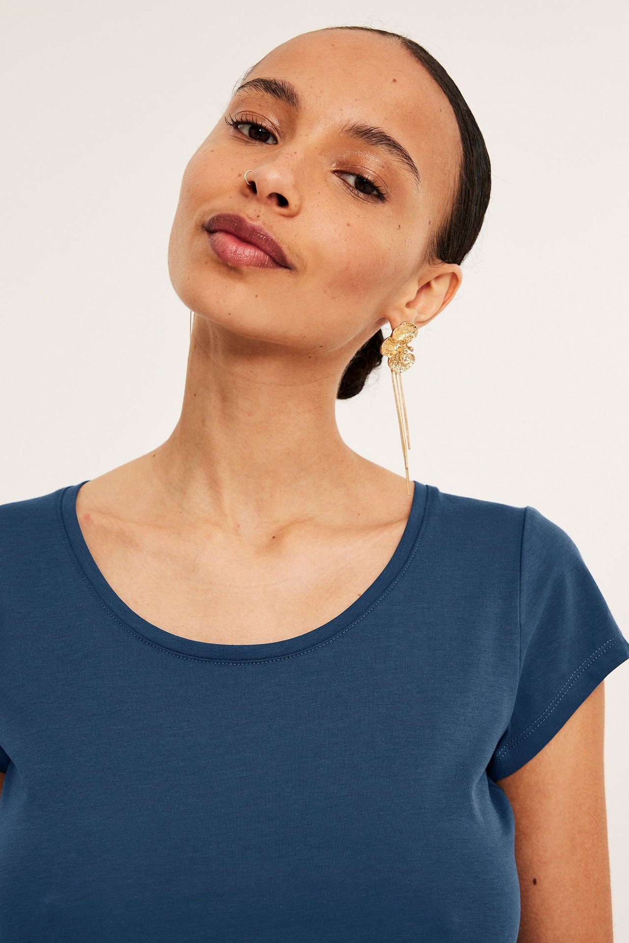 Nærbilde forfra: kvinne i en blå kortermet bomulls-t-skjorte med scoop-hals og gulløreringer.