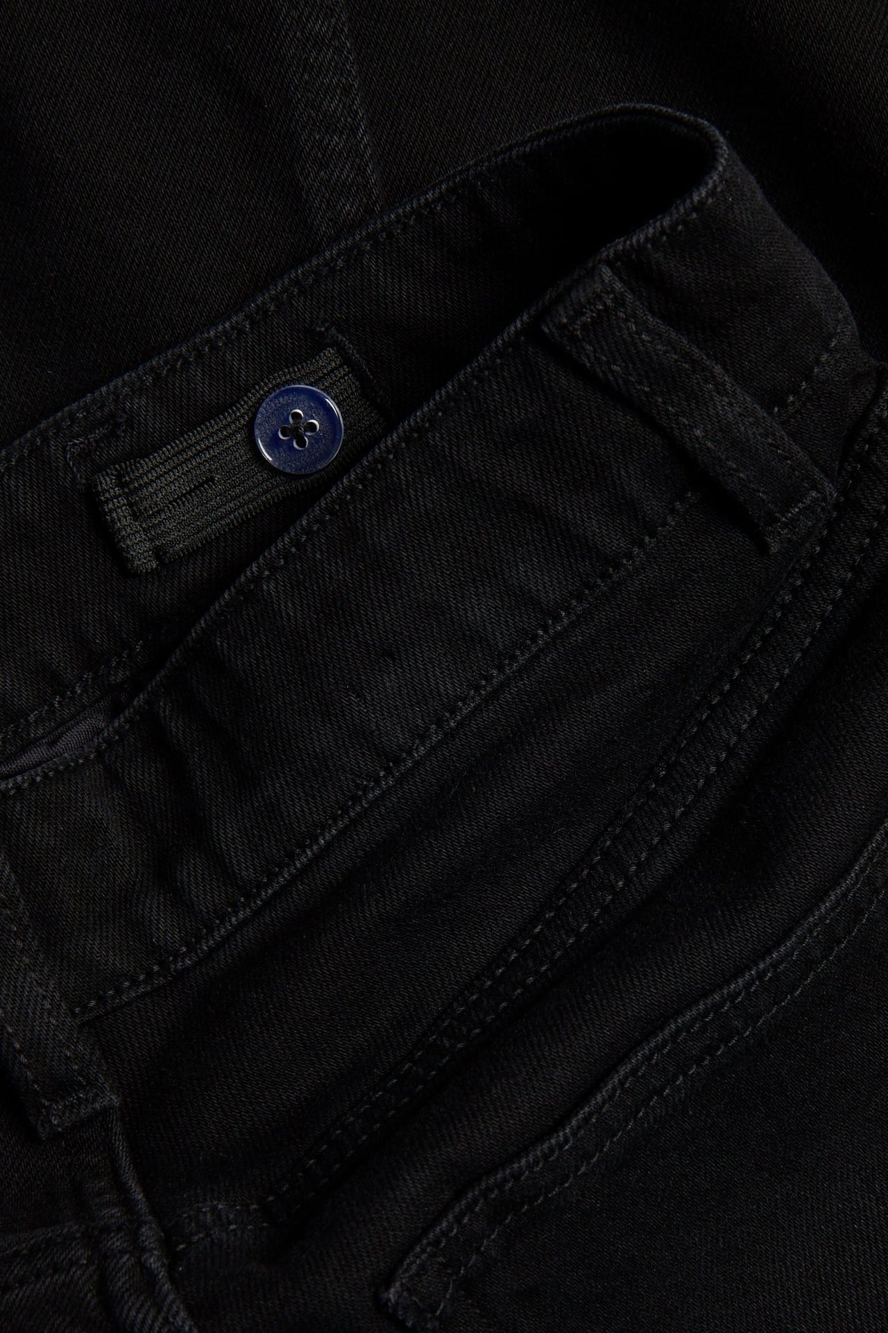 Zbliżenie czarnych luźnych jeansów denim z regulowaną gumką, średnim stanem i niebieskim guzikiem.