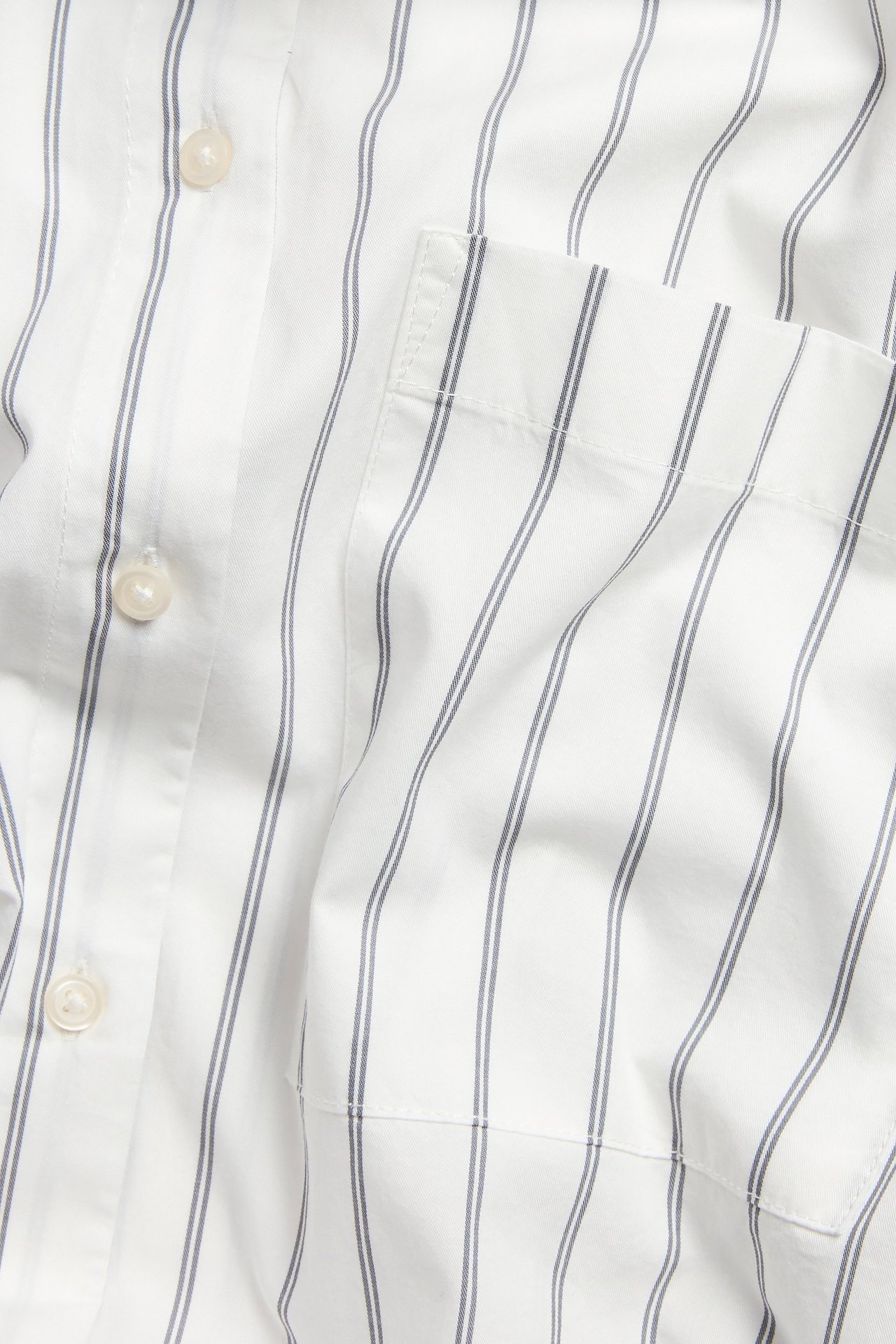 Zbliżenie na koszulę z białej bawełny popelinowej w pionowe niebieskie paski, z guzikami i kieszenią.