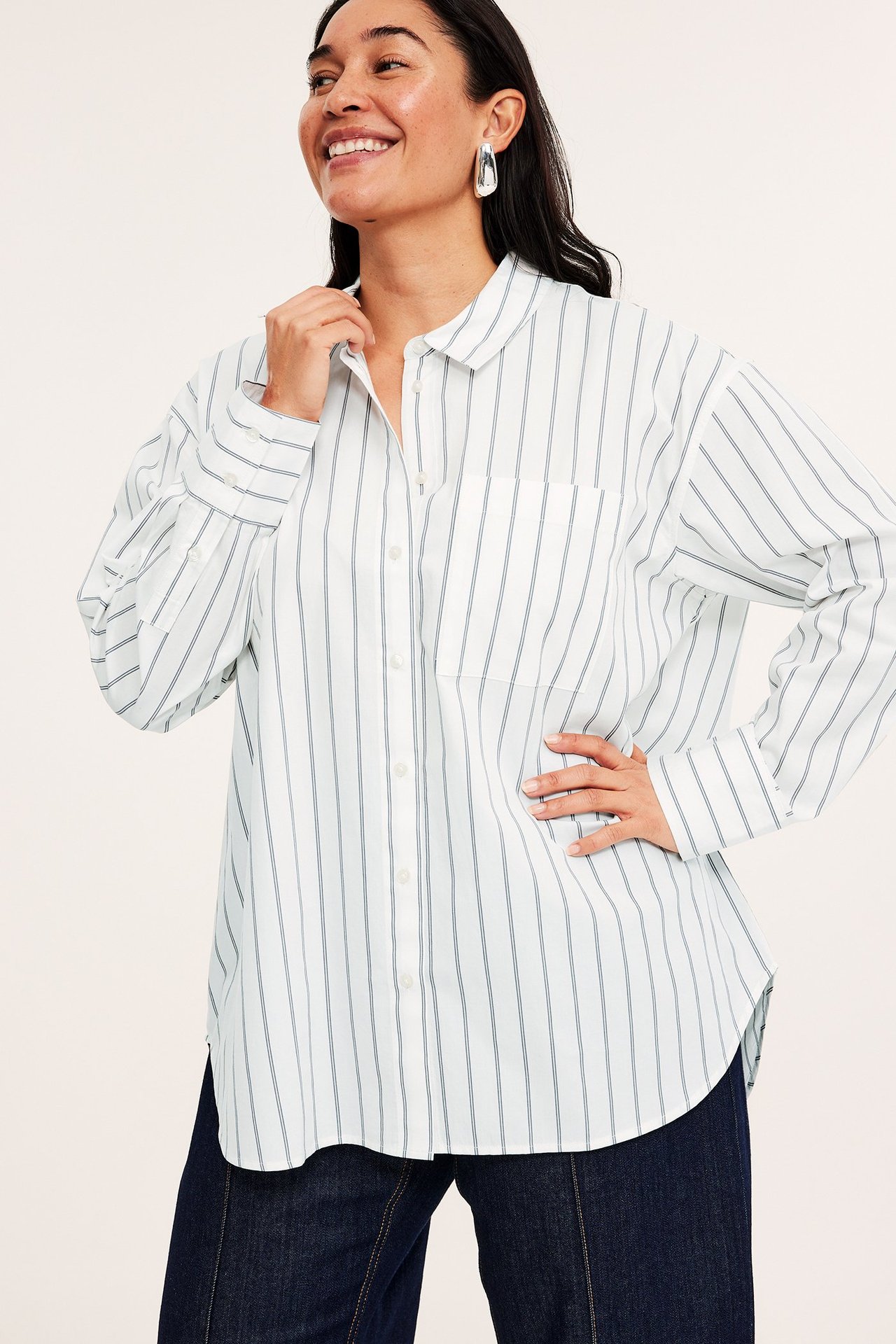 Widok z przodu: kobieta w ecru koszuli poplinowej w paski, ciemnych spodniach, srebrnych kolczykach.