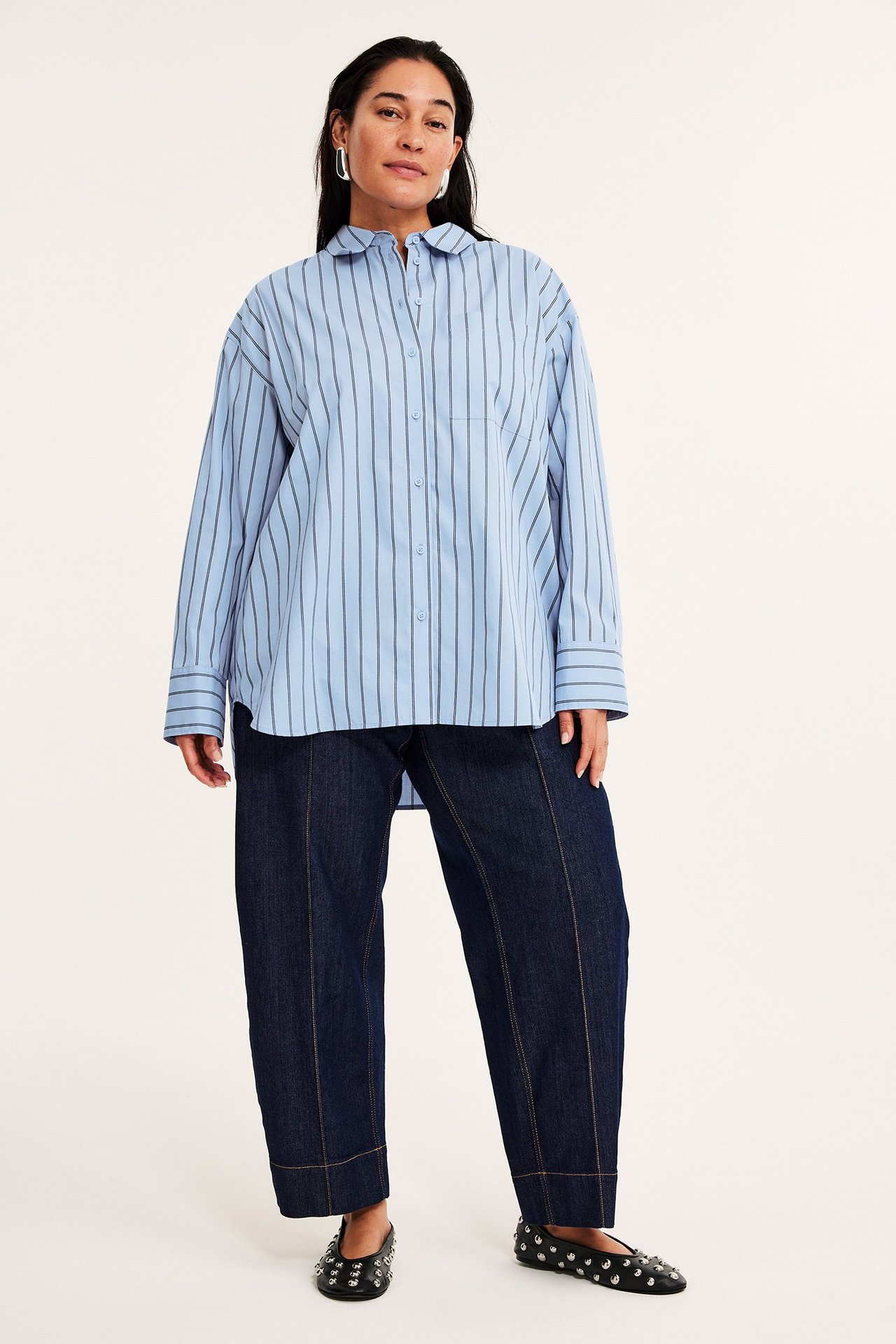 Framifrån: kvinna i ljusblå randig poplinskjorta, mörkblå byxor och svarta nitprydda ballerinaskor.