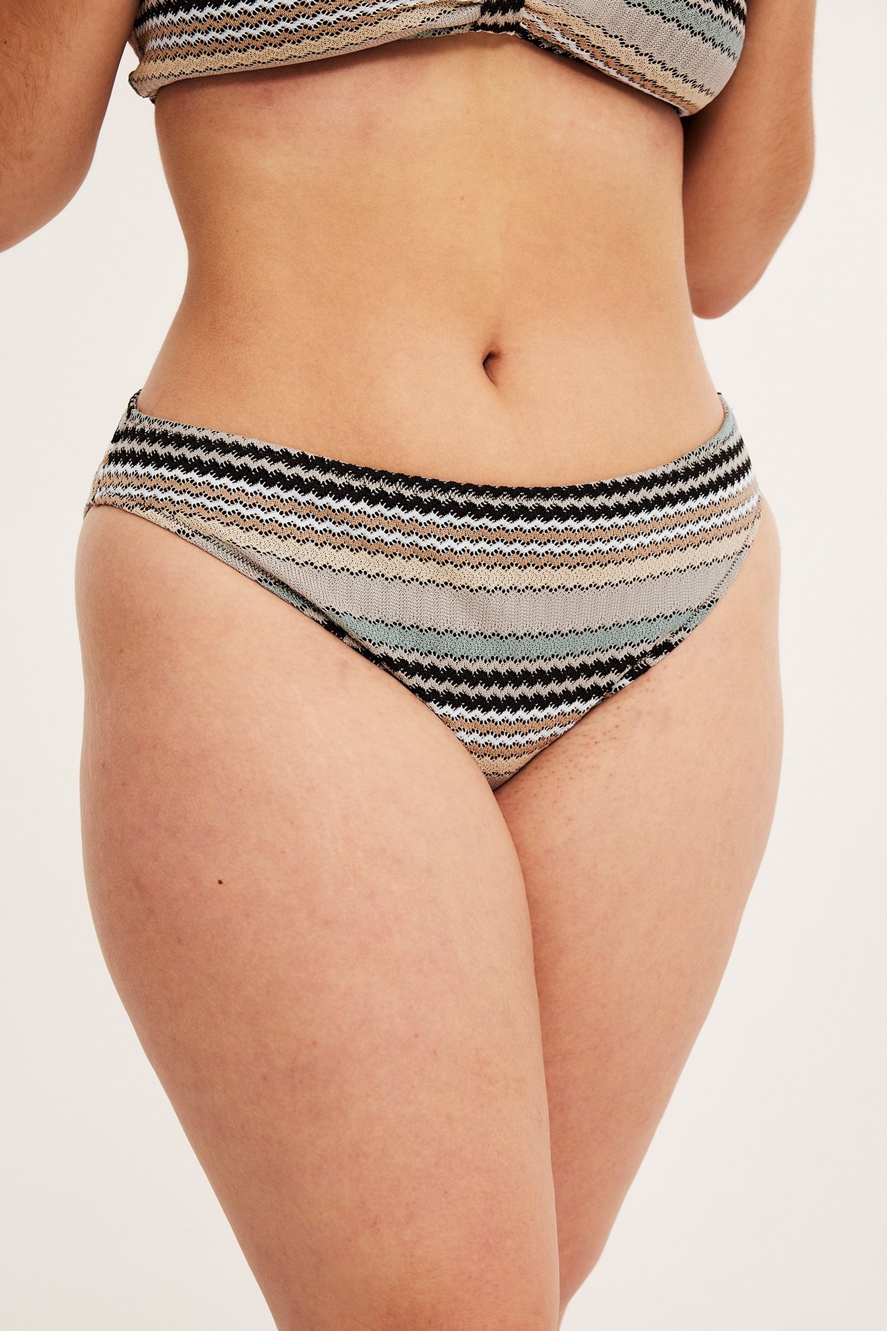 Frontbilde av kvinne i stripet bikinitruse med høyt ben i beige, svart, hvit og grønn.