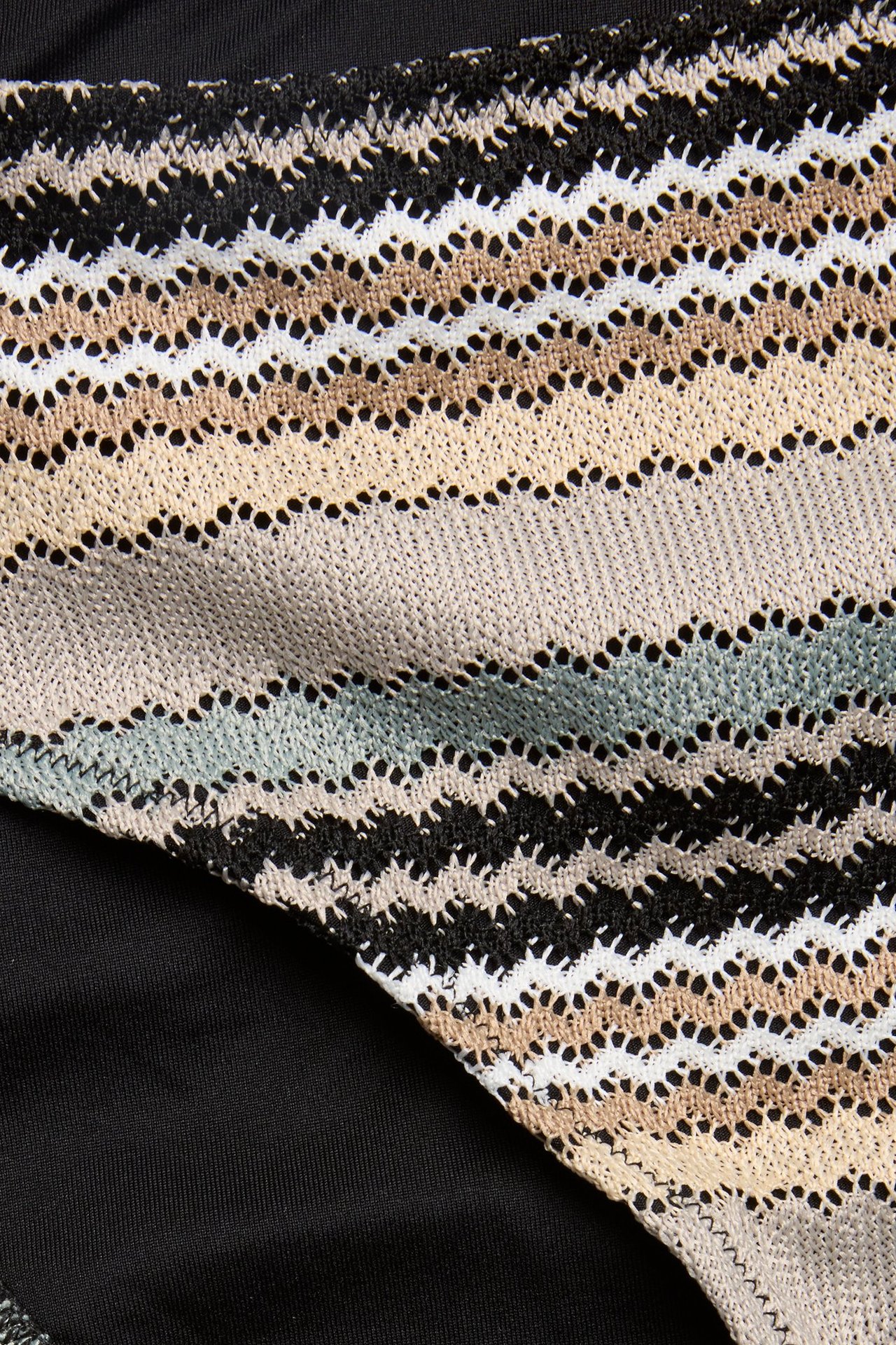 Zbliżenie na pasiasty dół bikini z czarnym, białym, beżowym i jasnoniebieskim wzorem w zygzak.