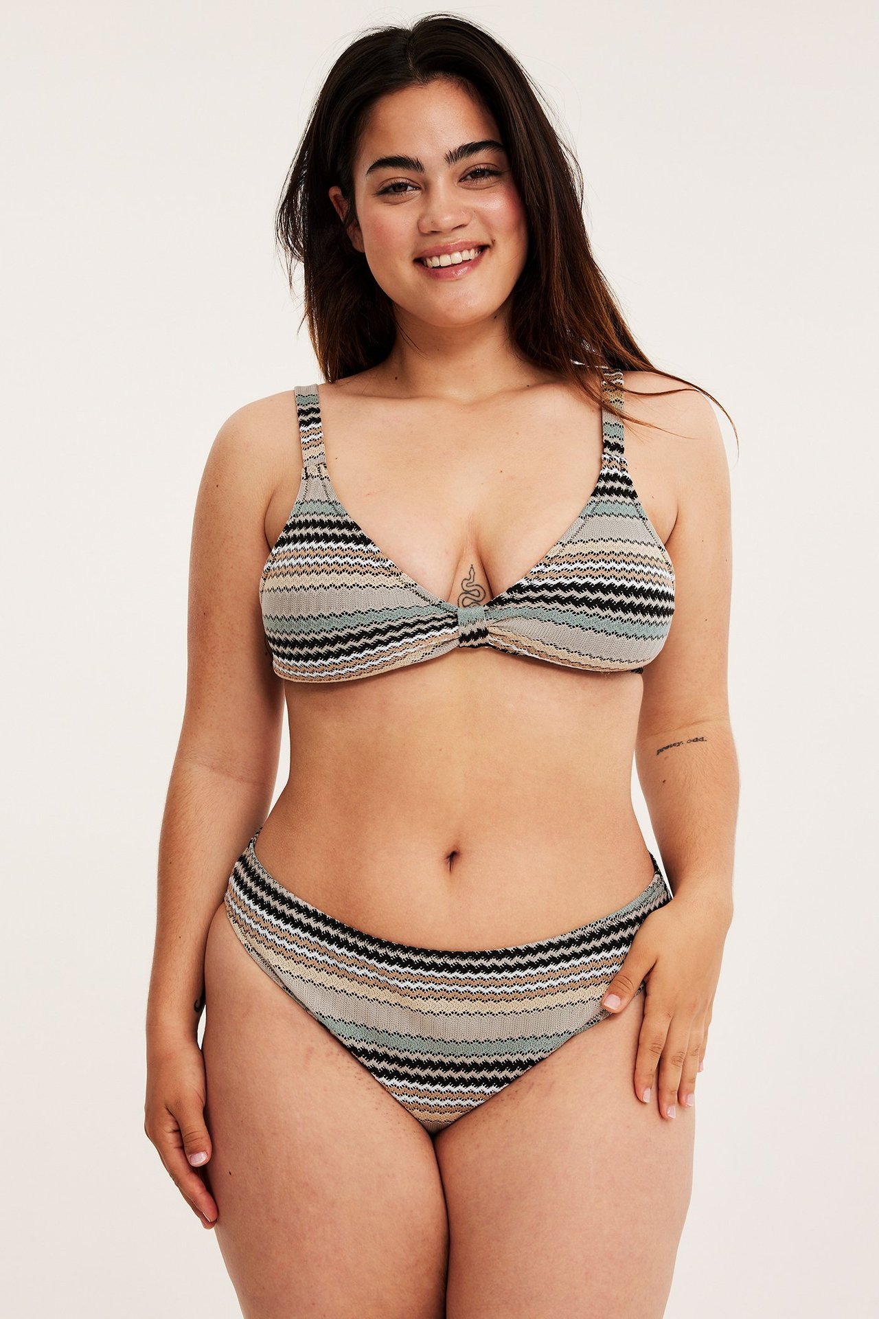 Kobieta z przodu w ciemnobeżowych, pasiastych majtkach bikini z wysokim stanem i pasującym topie.