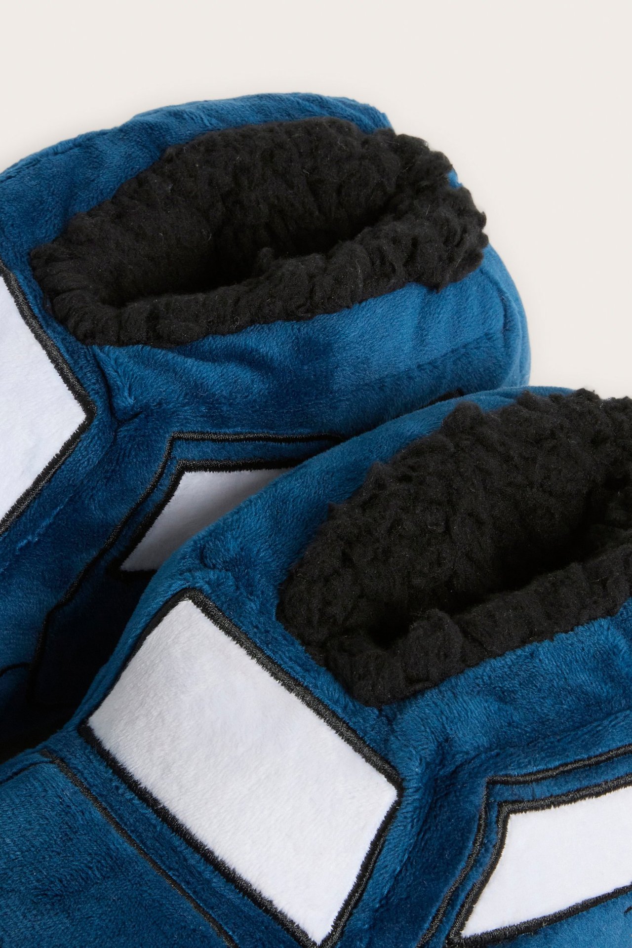 Lähikuva kahdesta sinisestä autonmuotoisesta lasten tossusta, joissa musta fleecevuori ja valkoiset yksityiskohdat.