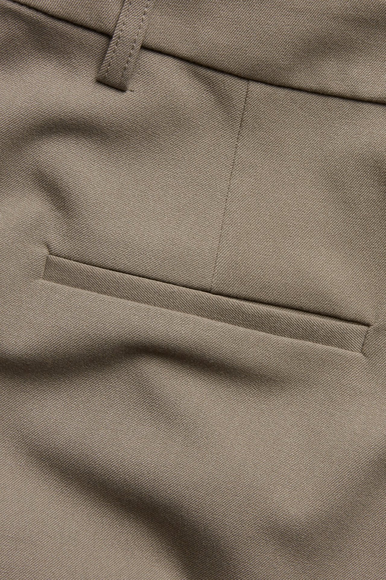 Zbliżenie beżowo-brązowych spodni garniturowych, ukazujące fakturę materiału, szlufkę i kieszeń.