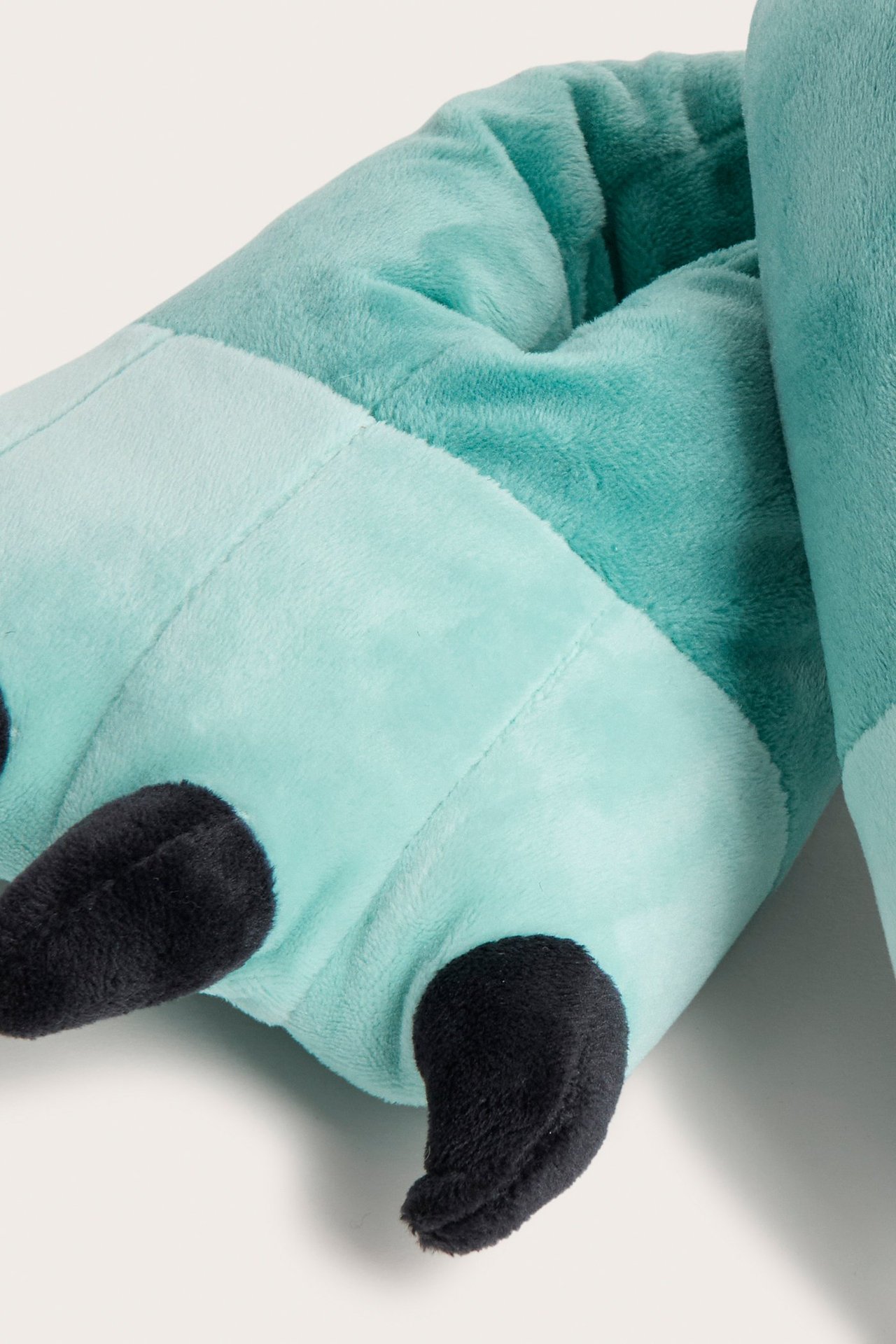 Lähikuva pehmeästä vihreästä lasten tossusta, jossa on mustat kynnet, valmistettu muhkeasta polyesteristä.