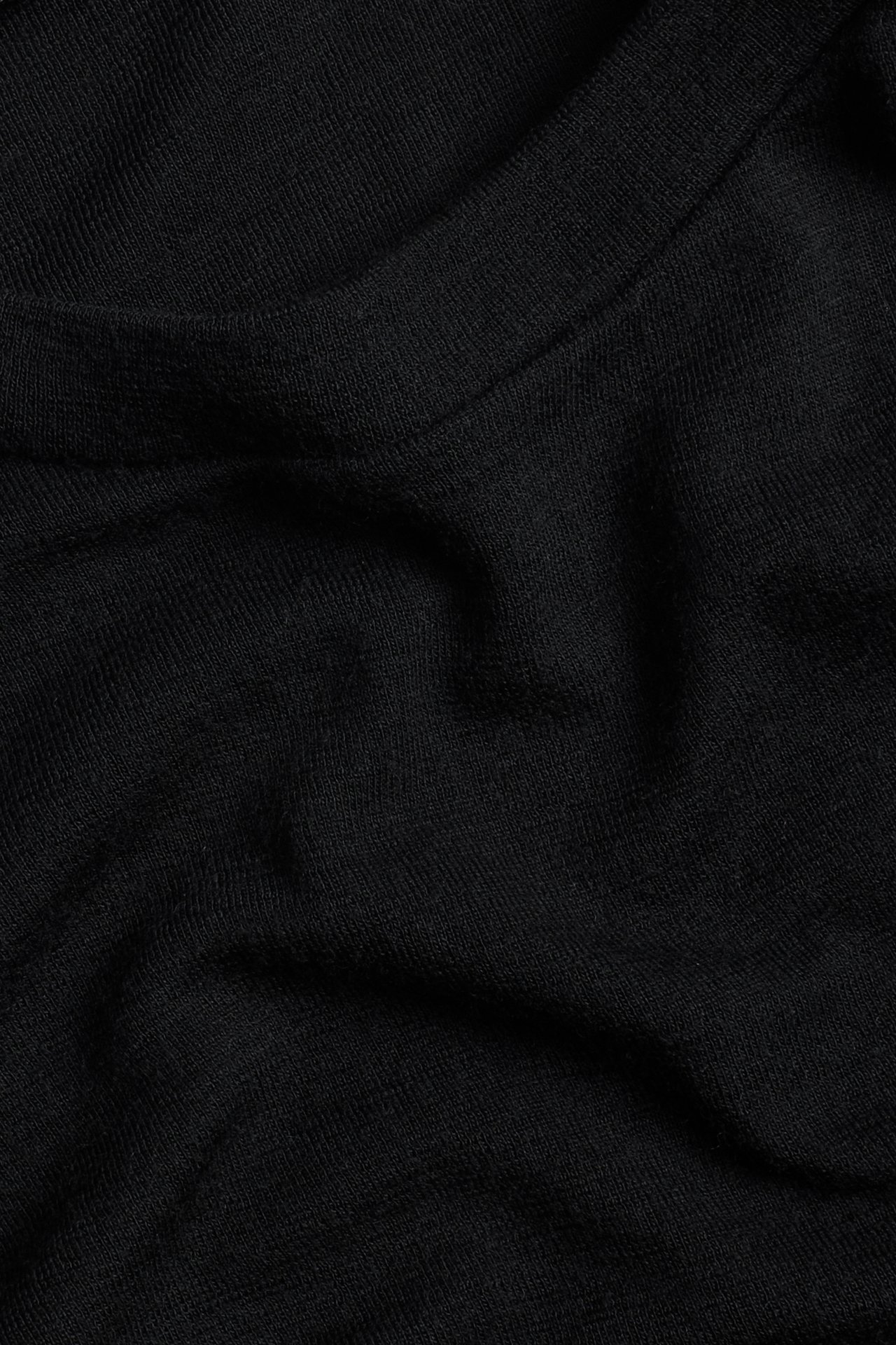 Närbild av svart stickat tyg med synlig textur och diskreta veck.
