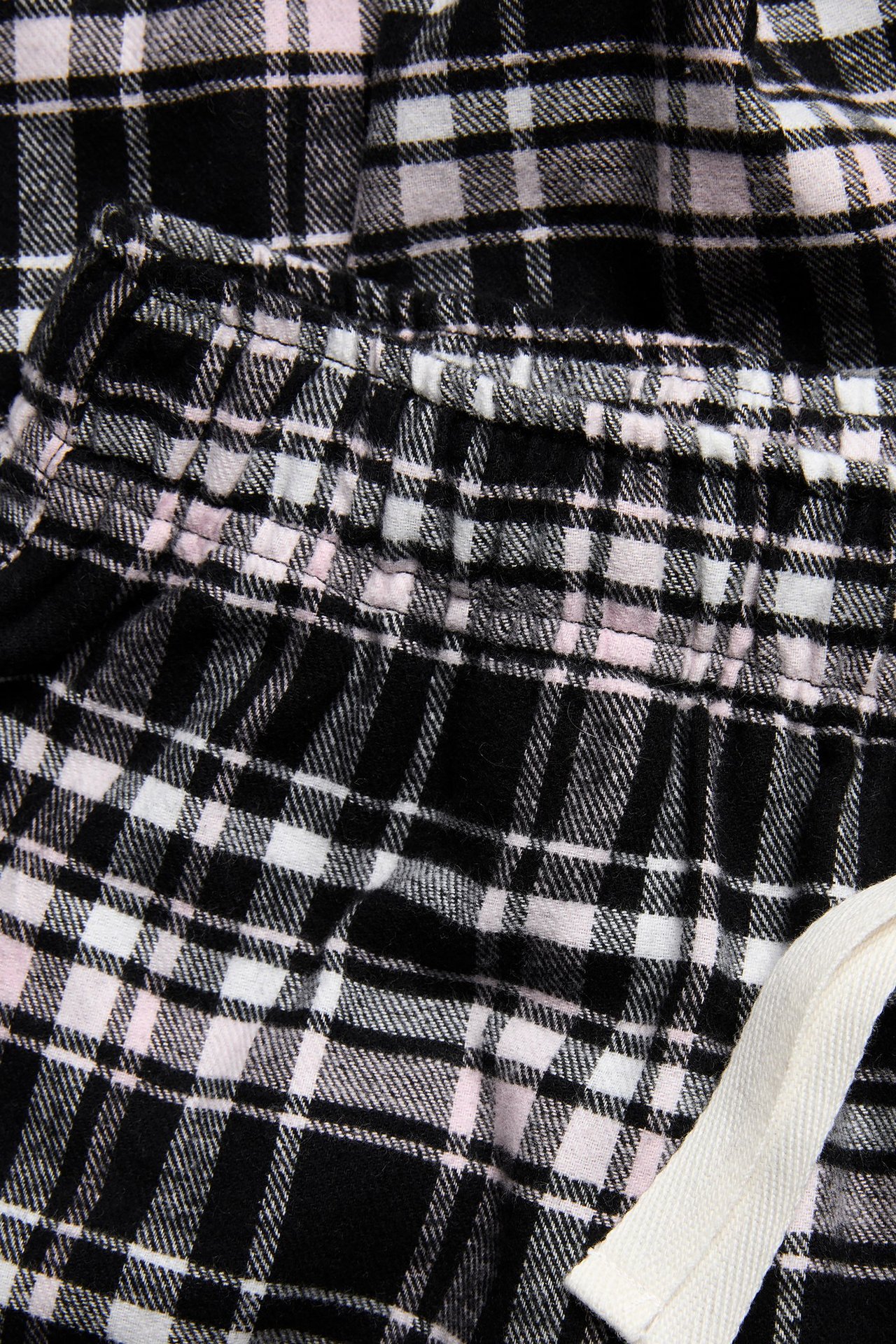Zbliżenie na czarno-biało-różowe flanelowe spodnie piżamowe w kratę z elastycznym pasem i sznurkiem.