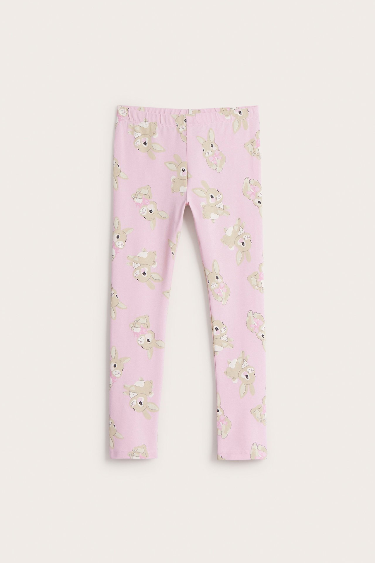 Edestä: lasten vaaleanpunaiset slim-fit leggingsit, joissa pupukuvio; joillakin pupuilla on rusetit.