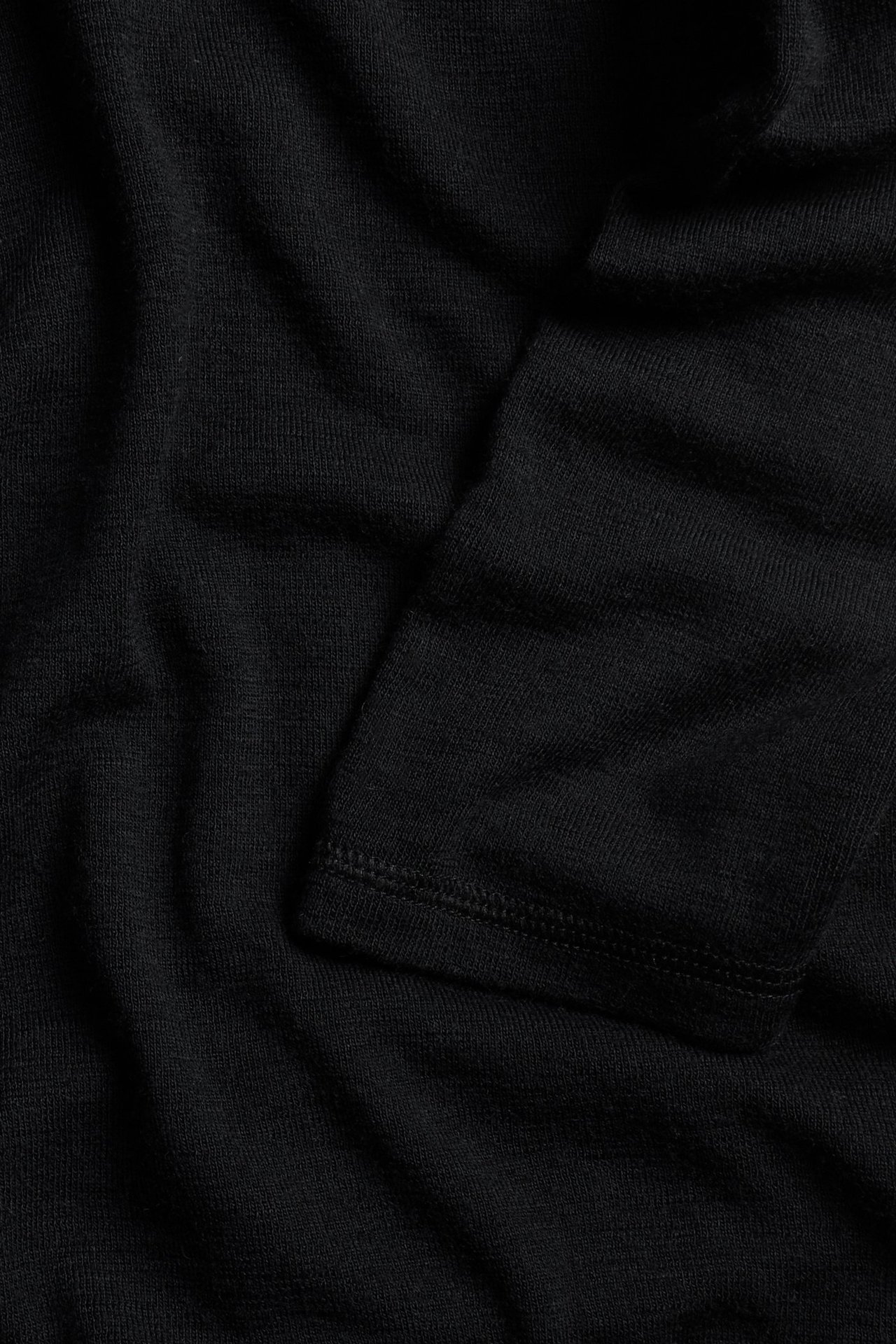 Zbliżenie czarnego golfu z wełny merynosów z widocznym mankietem rękawa.