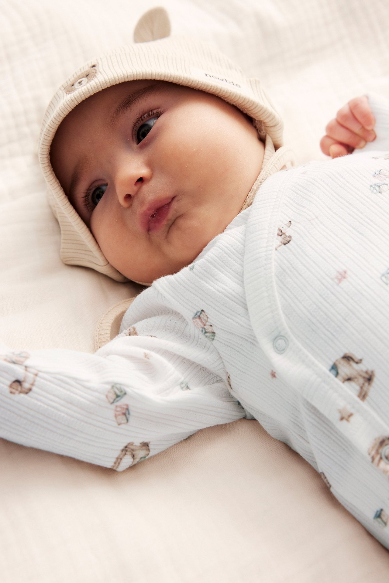 Närbild på baby i offwhite ribbad omlottbody med leksaksmönster och matchande mössa med björnöron.