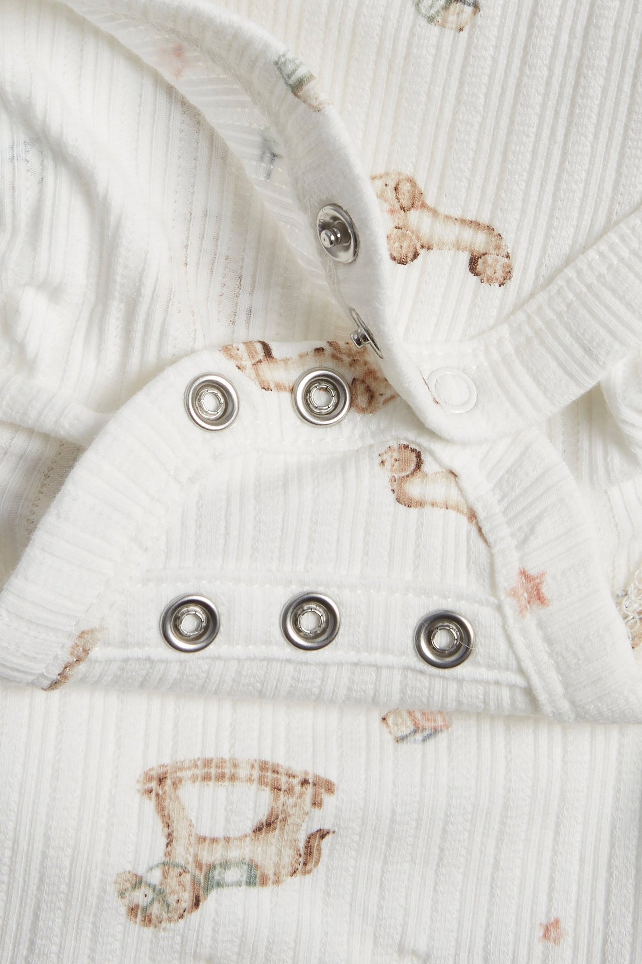 Närbild på en offwhite ribbad omlottbody för baby med leksaksmönster och tryckknappar.