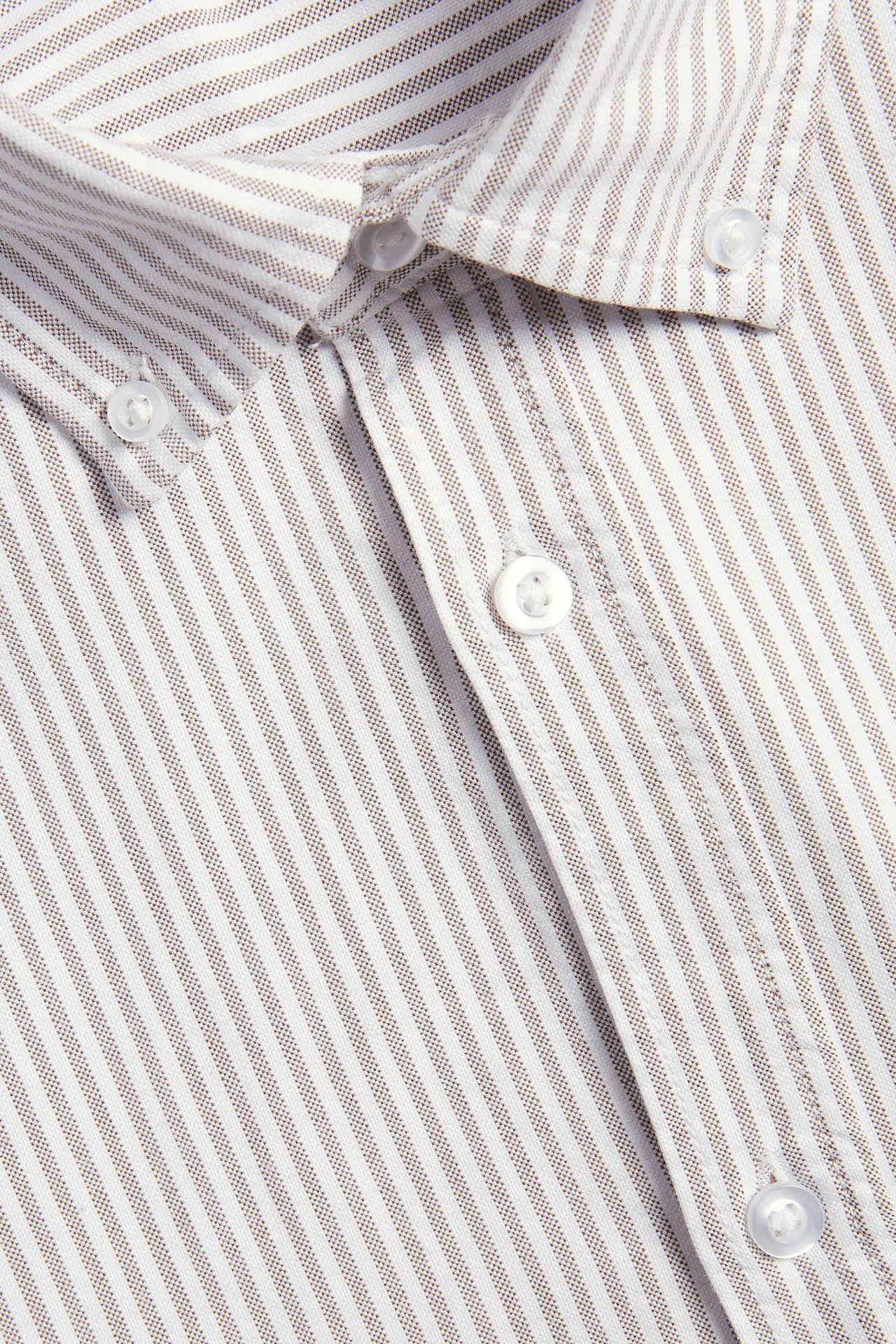 Zbliżenie na brązowo-białą koszulę oxford w paski, z bawełny, z kołnierzykiem button-down i białymi guzikami.