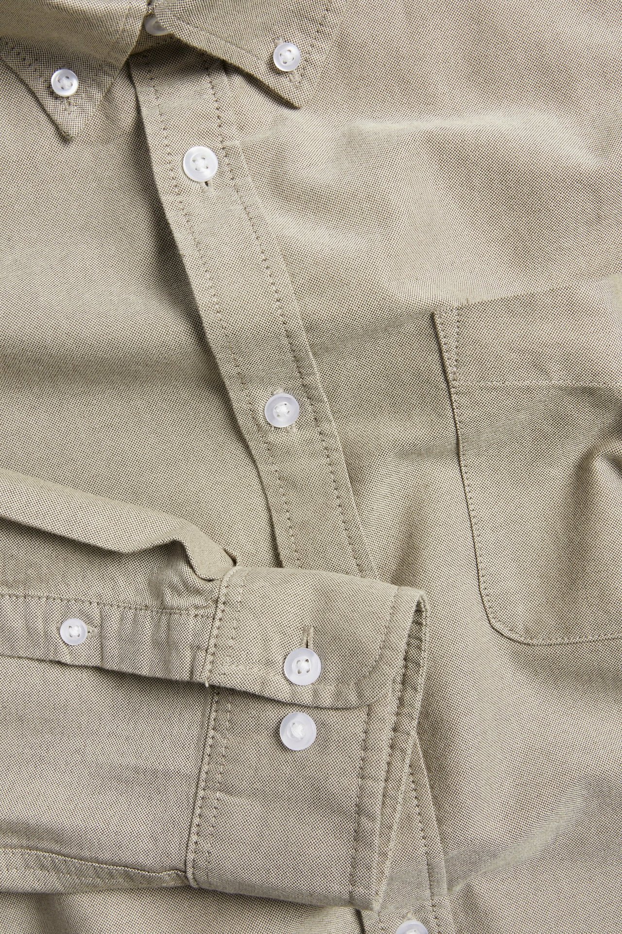 Zbliżenie na brązową melanżową koszulę Oxford z bawełny, z kołnierzykiem button-down, kieszenią i białymi guzikami.