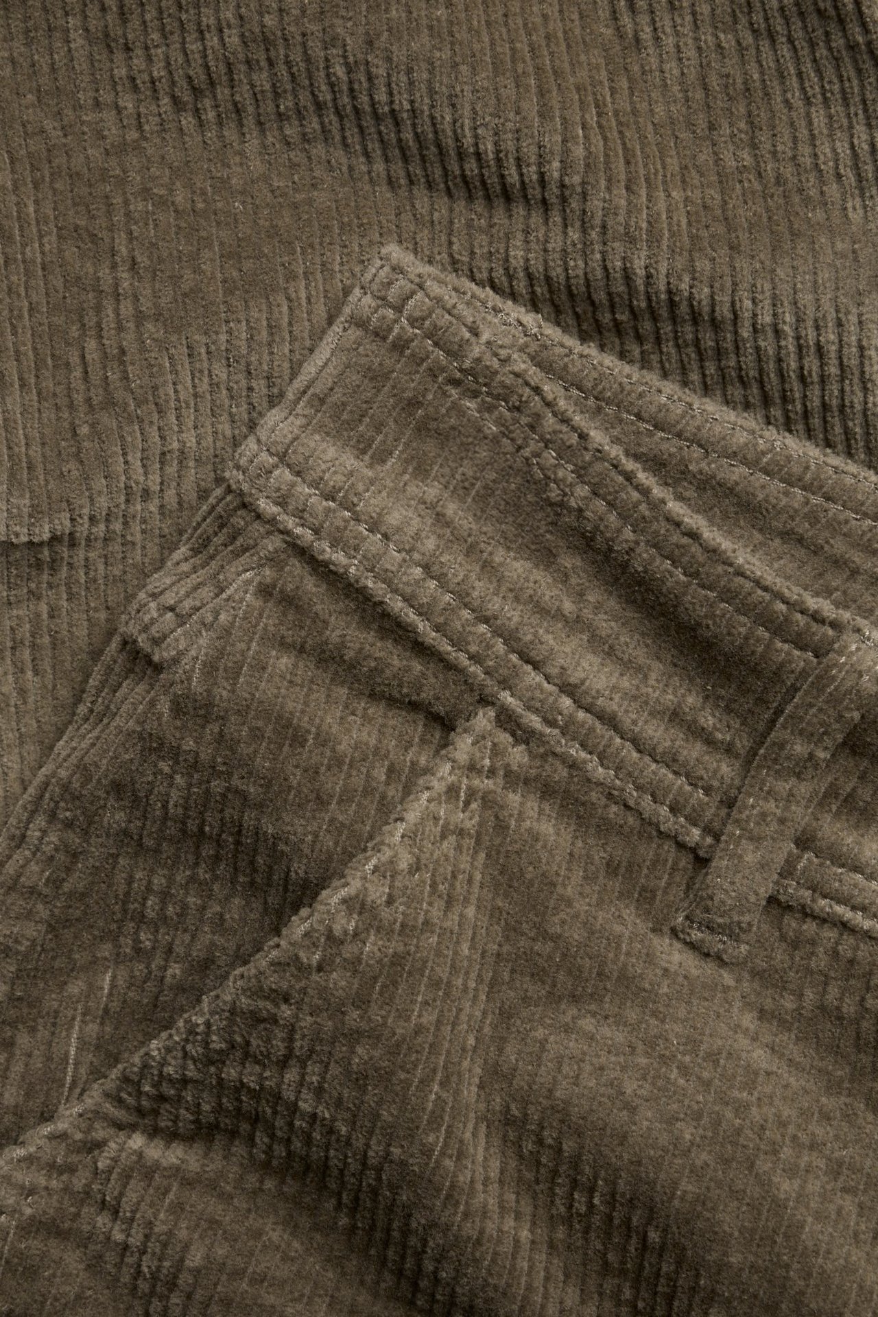 Zbliżenie jasnobrązowych sztruksowych spodni, ukazujące pas, szlufki i detal kieszeni.