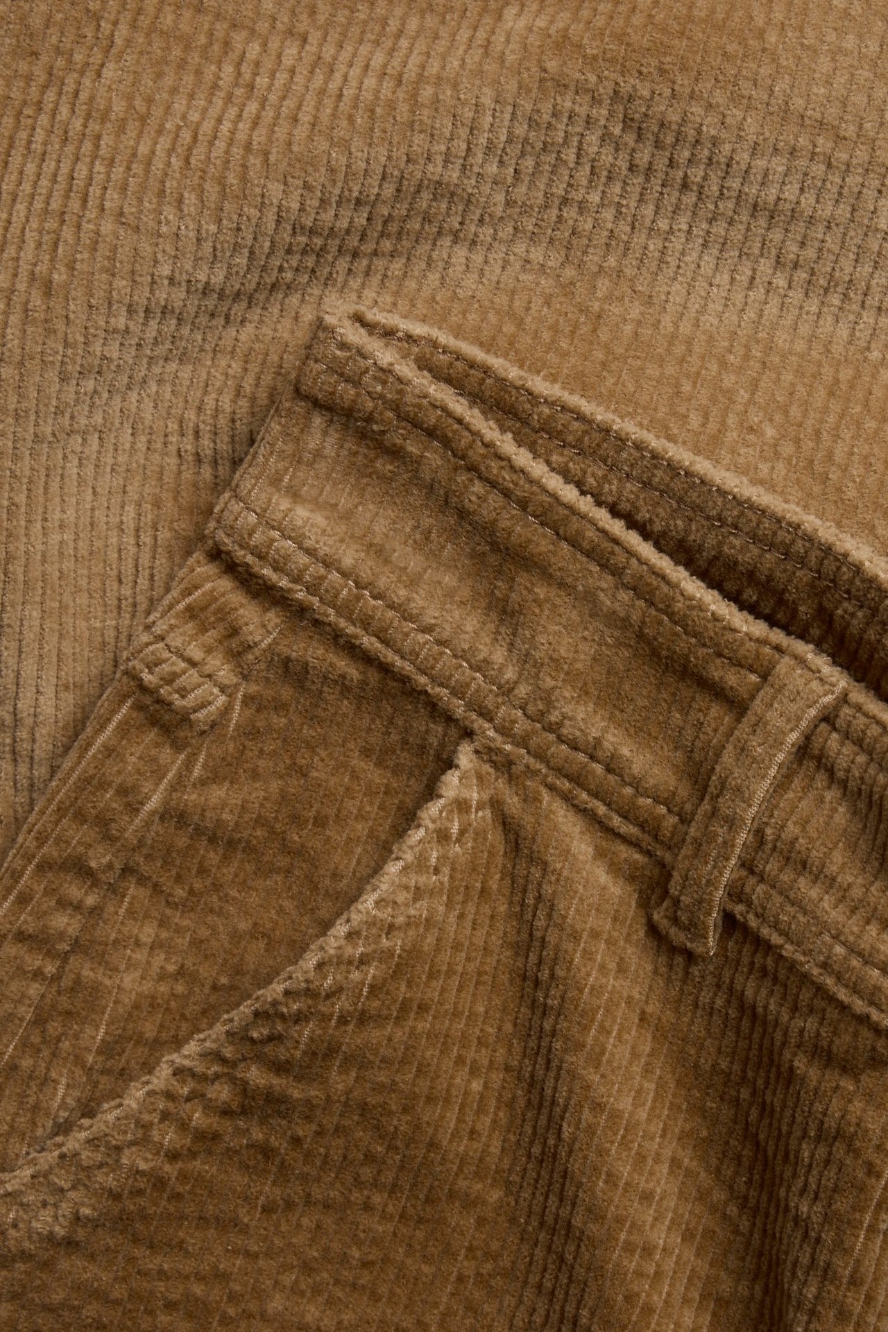 Zbliżenie beżowych sztruksowych spodni, ukazujące prążkowany materiał, kieszeń i szlufki.