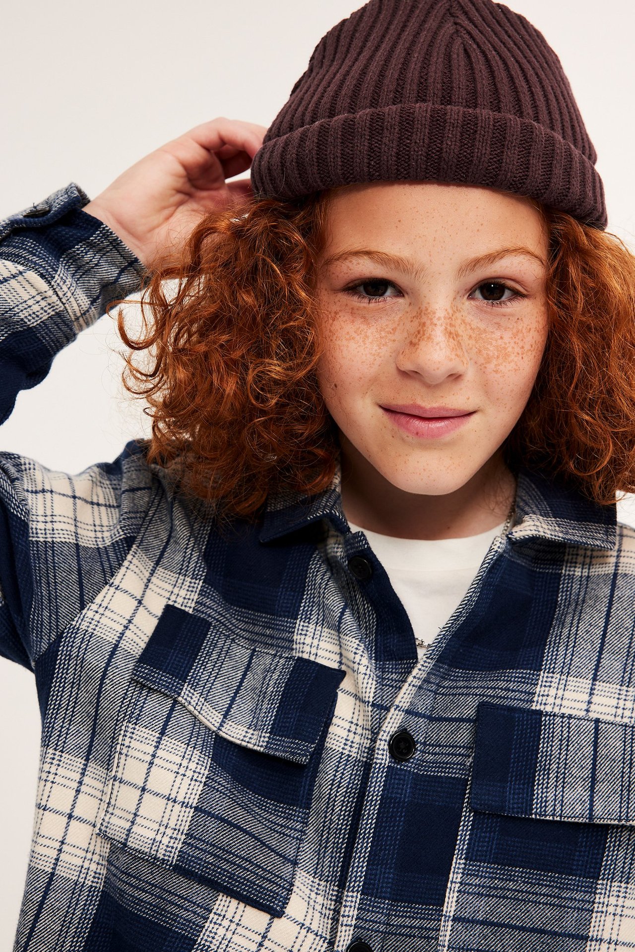Zbliżenie dziecka w ciemnoczerwonej prążkowanej czapce beanie i koszuli w granatowo-kremową kratę.