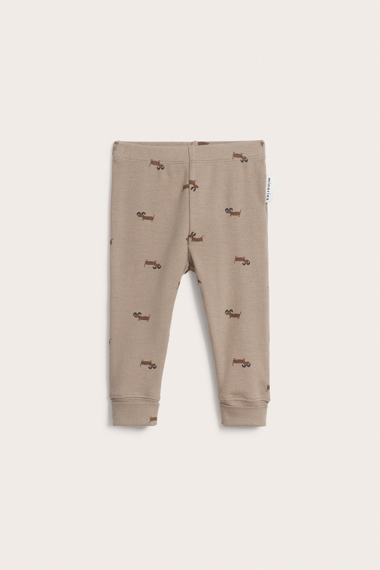 Framifrån: Ljusbruna ribbade babyleggings med brunt hundmönster och resår i midjan.
