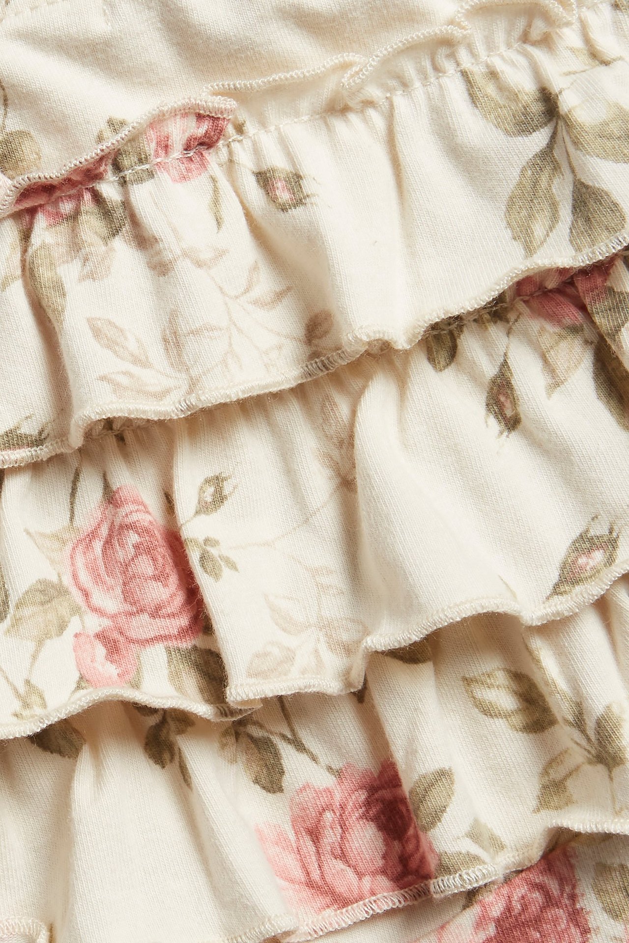 Lähikuva vaaleanbeigestä kukkakuvioisesta leggingseistä, joissa on vaaleanpunaisia ruusuja ja röyhelöitä.