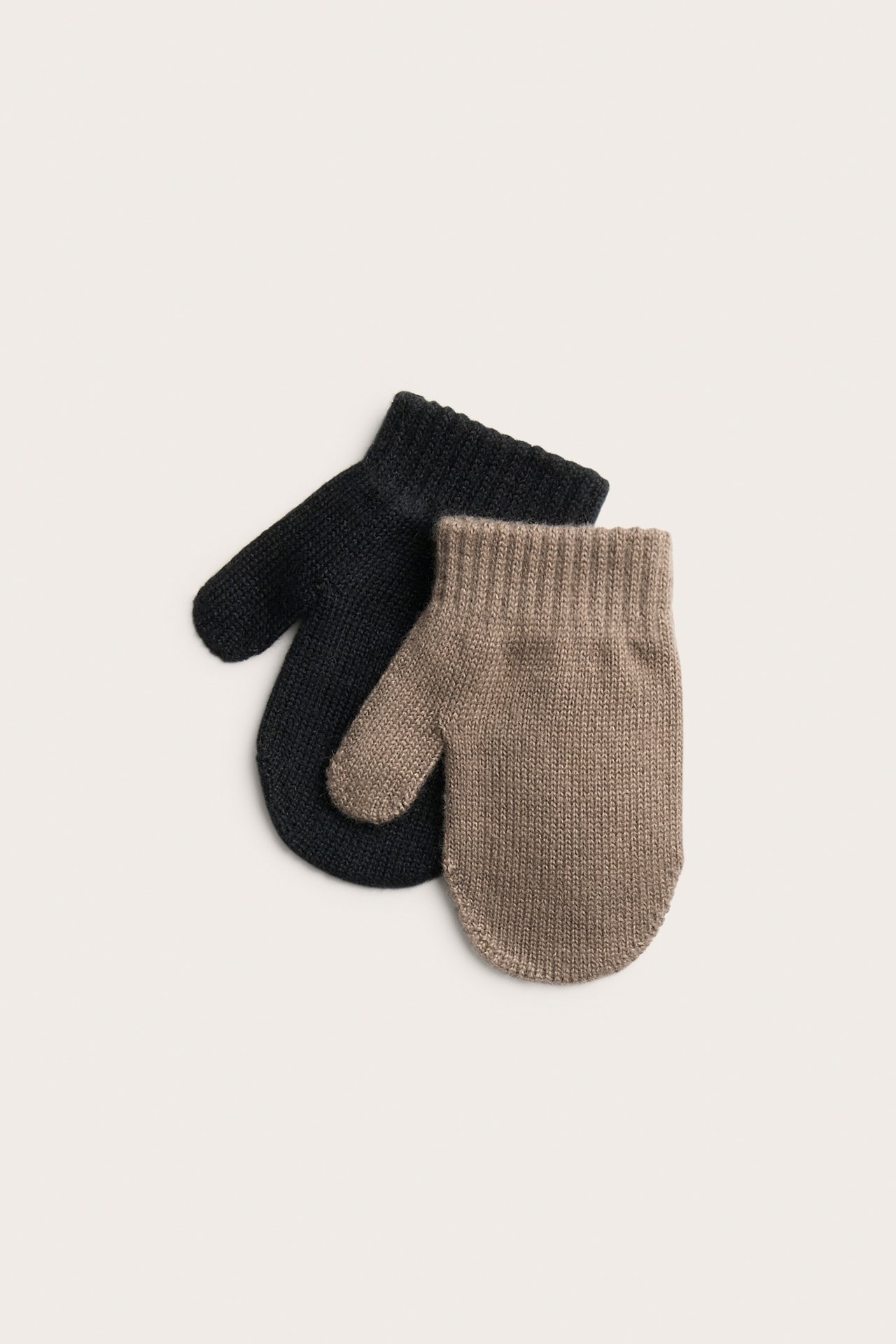 Uppifrån sett, en beige stickad babyvante över en svart stickad babyvante.