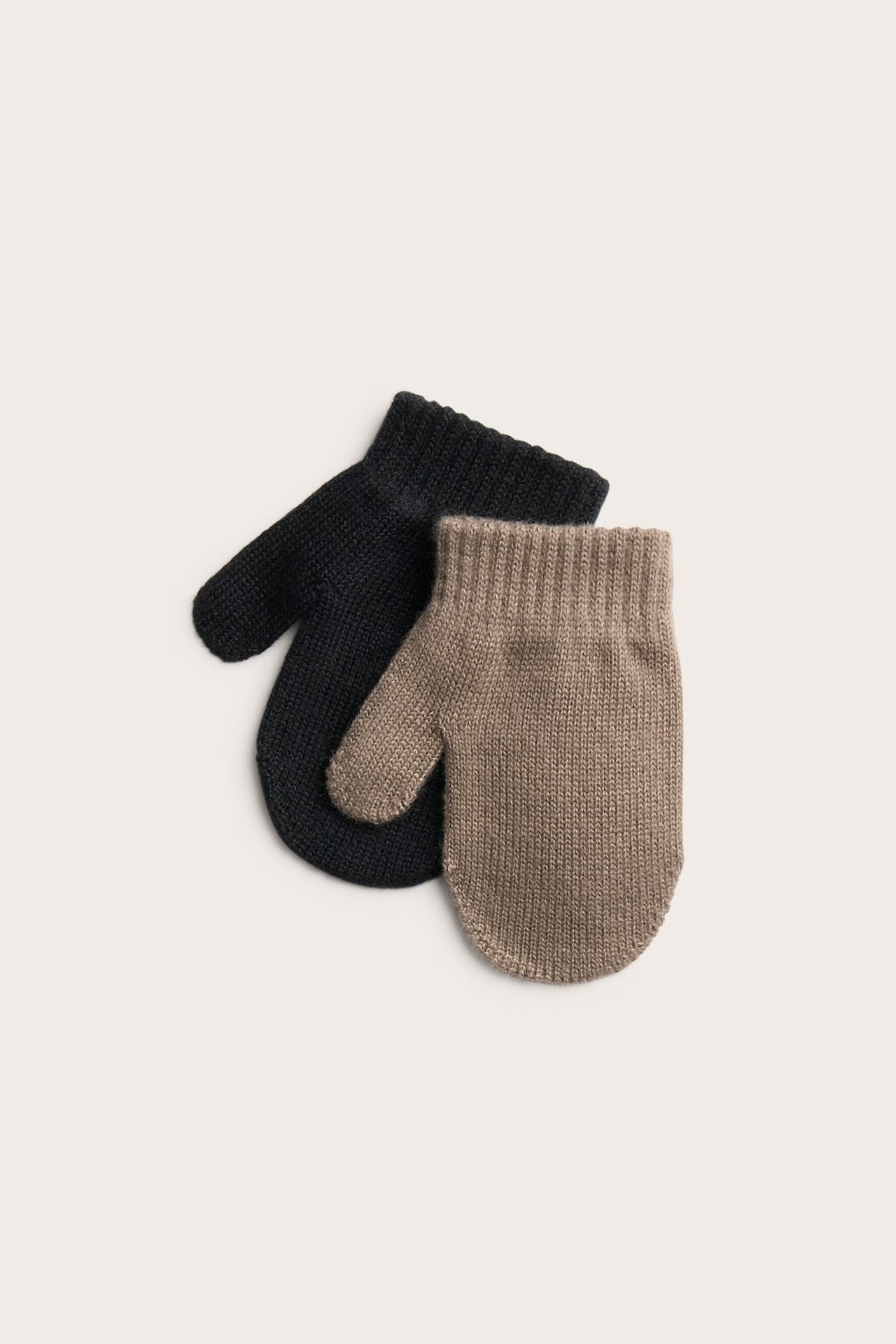 Ylhäältä näkymä, beige neulottu vauvan lapanen mustan neulotun vauvan lapasen päällä.