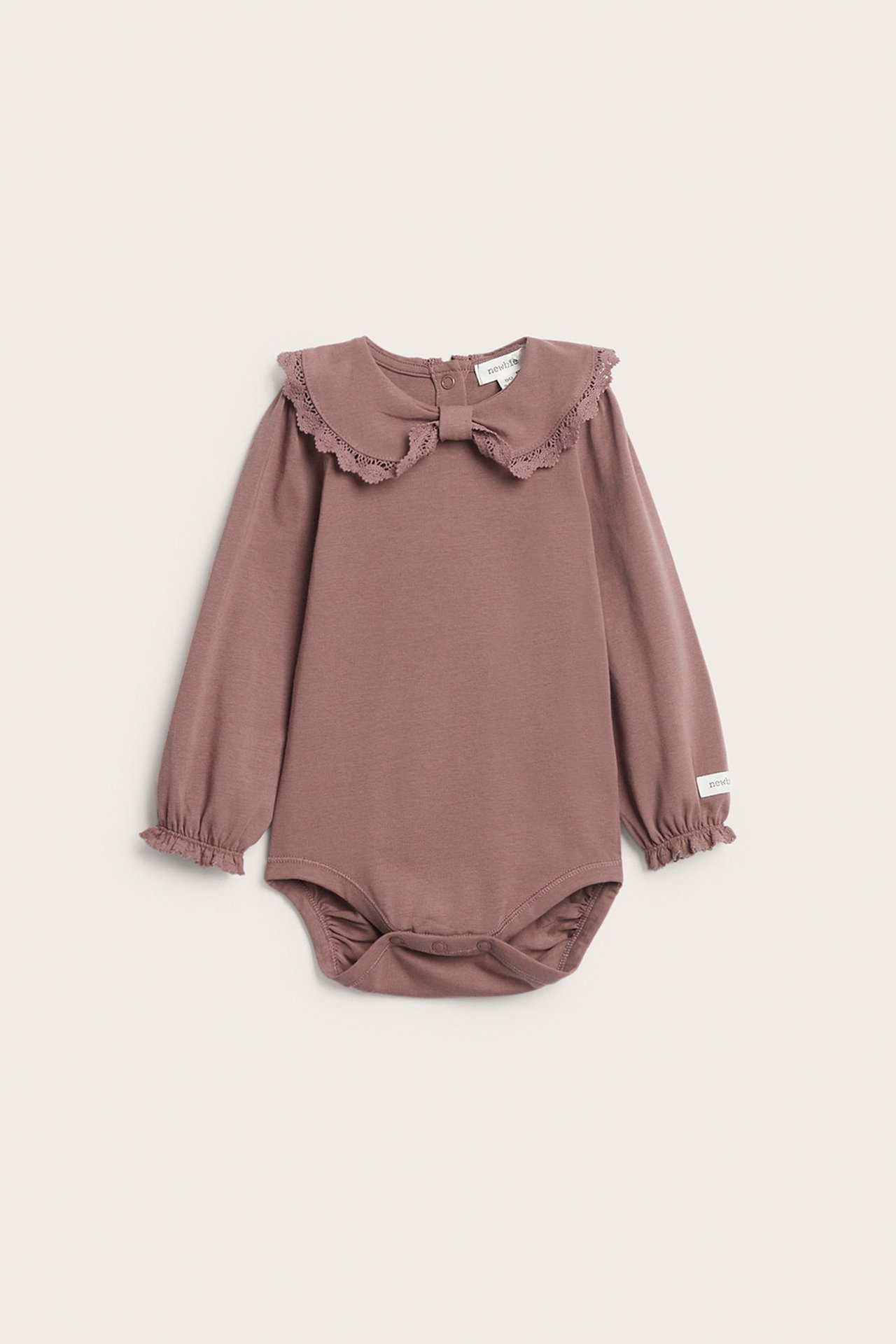 Frontvy av en mörkrosa babybody med spetskantad rosettkrage och volangärmslut, tryckknappar.