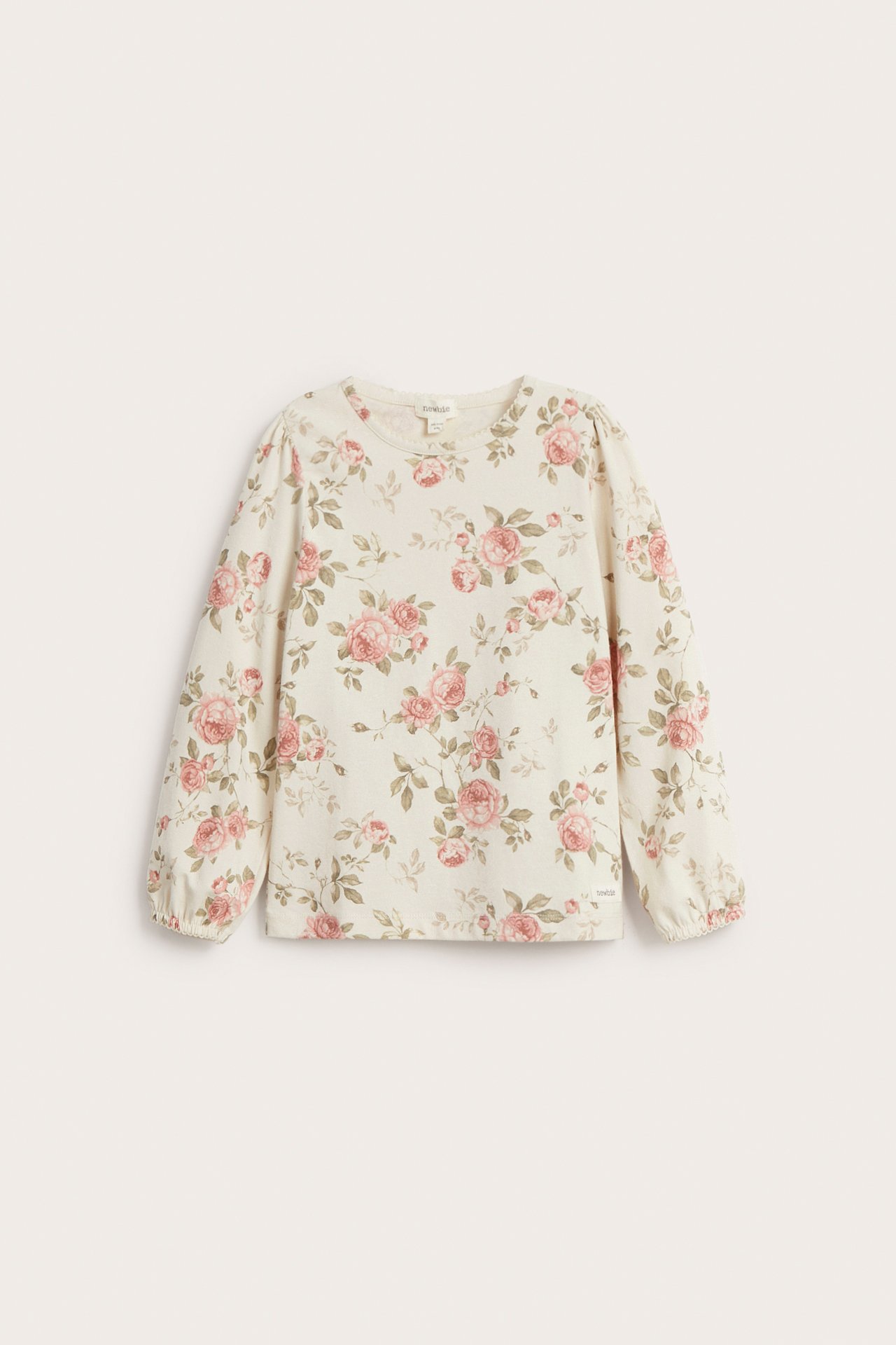 Frontvisning av en lys beige bomullstopp med rosa blomstermønster, puffermer og picotkant.