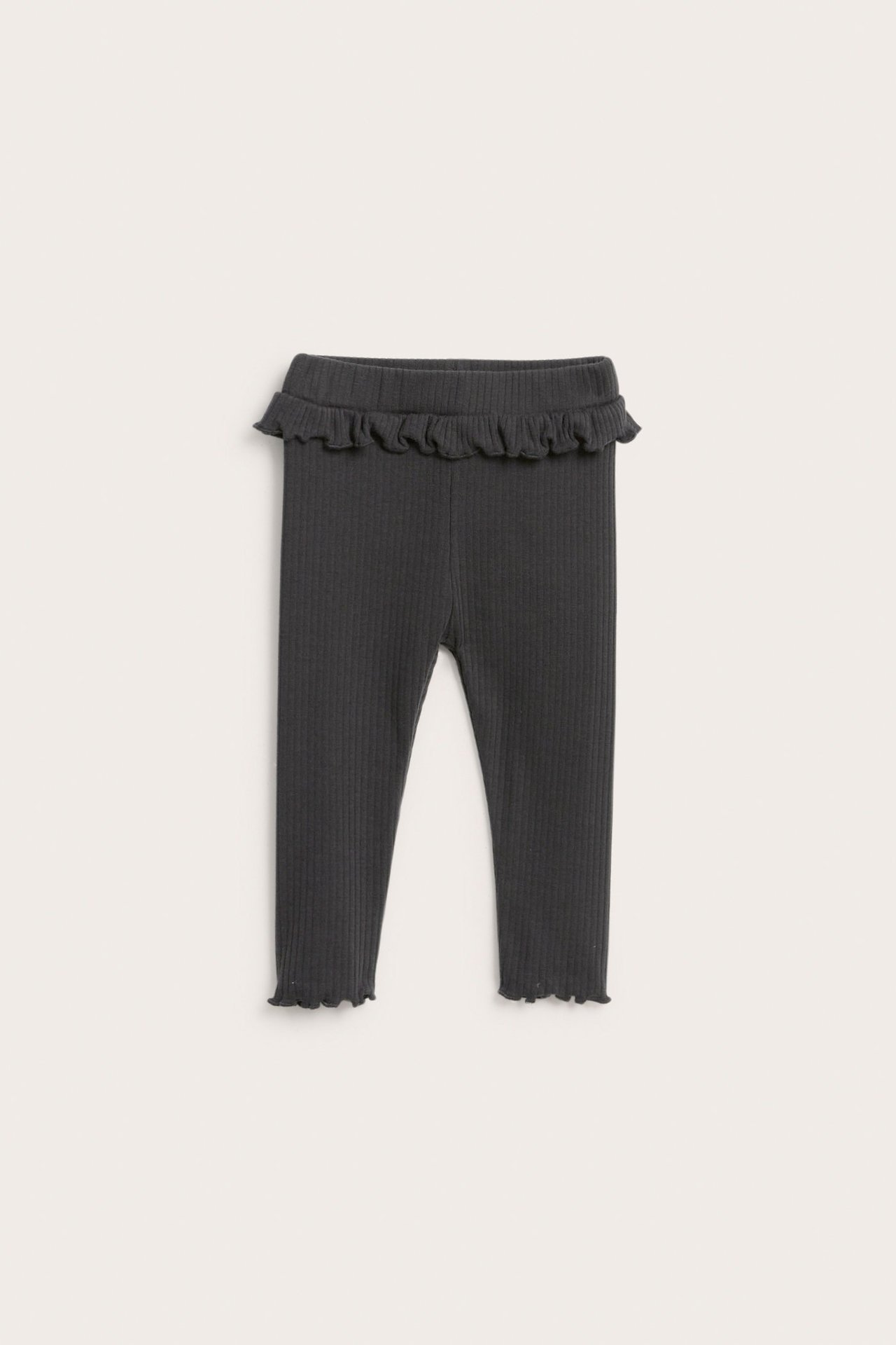 Frontvy av svarta ribbade baby leggings med volangdetalj i midjan och volangfållar.