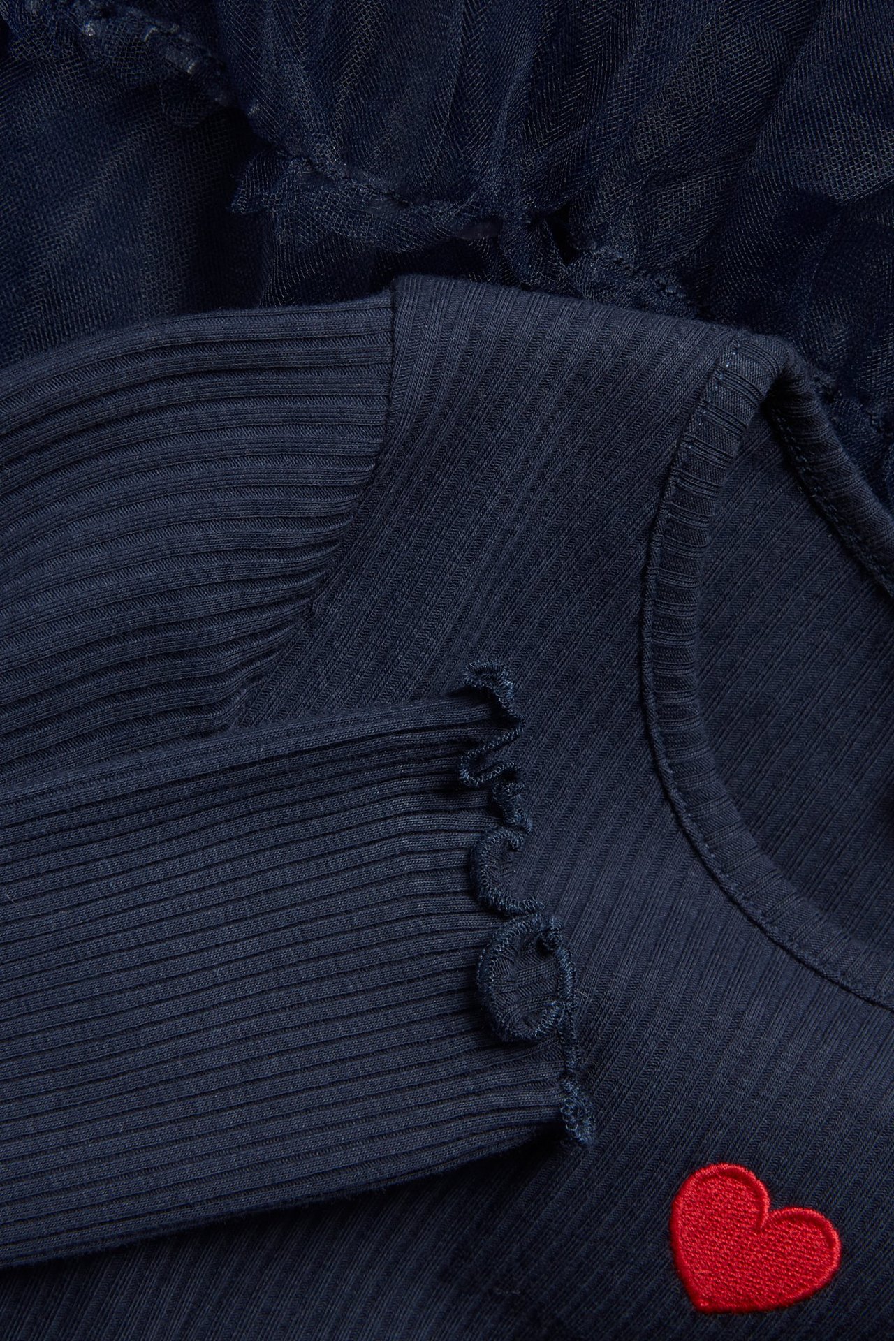 Zbliżenie granatowej prążkowanej sukienki dziecięcej z tiulową spódnicą i małym czerwonym sercem.