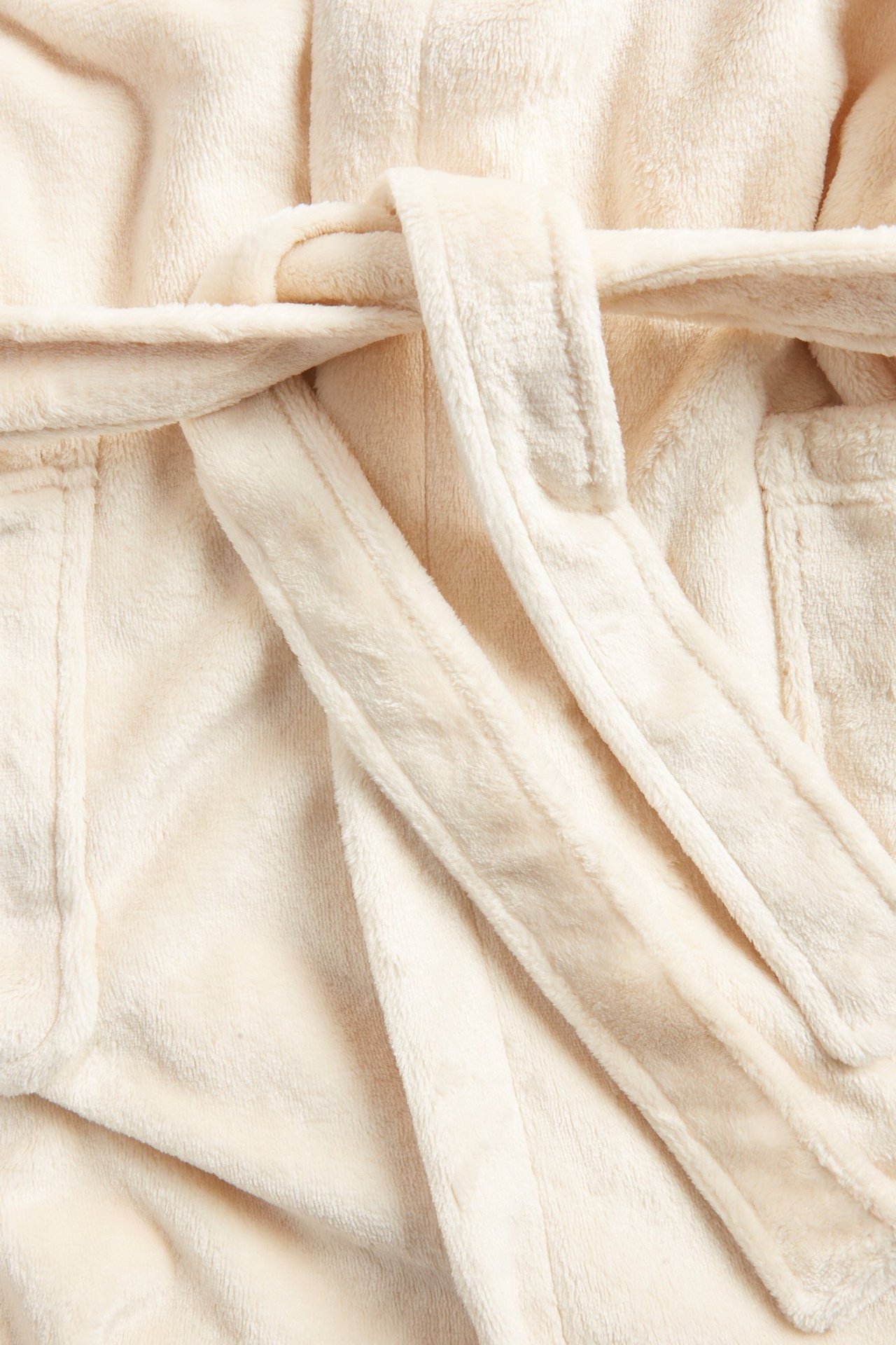 Zbliżenie na jasnobeżowy szlafrok polarowy z wiązanym paskiem i widocznymi detalami kieszeni.
