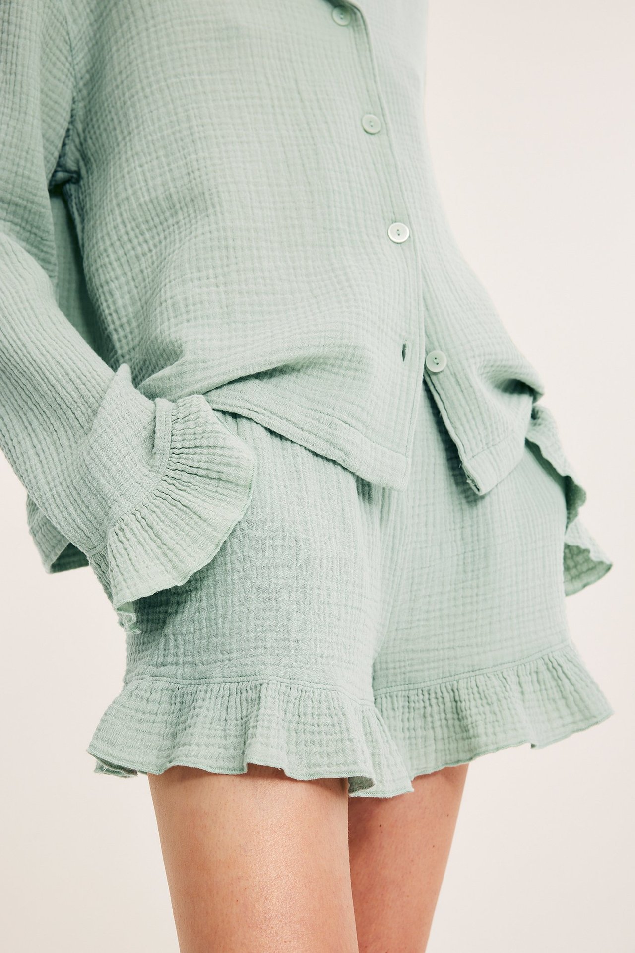 Lähikuva edestä naisesta, jolla on vaaleanvihreät rypytetyt puuvillapyjamashortsit ja yhteensopiva paita.