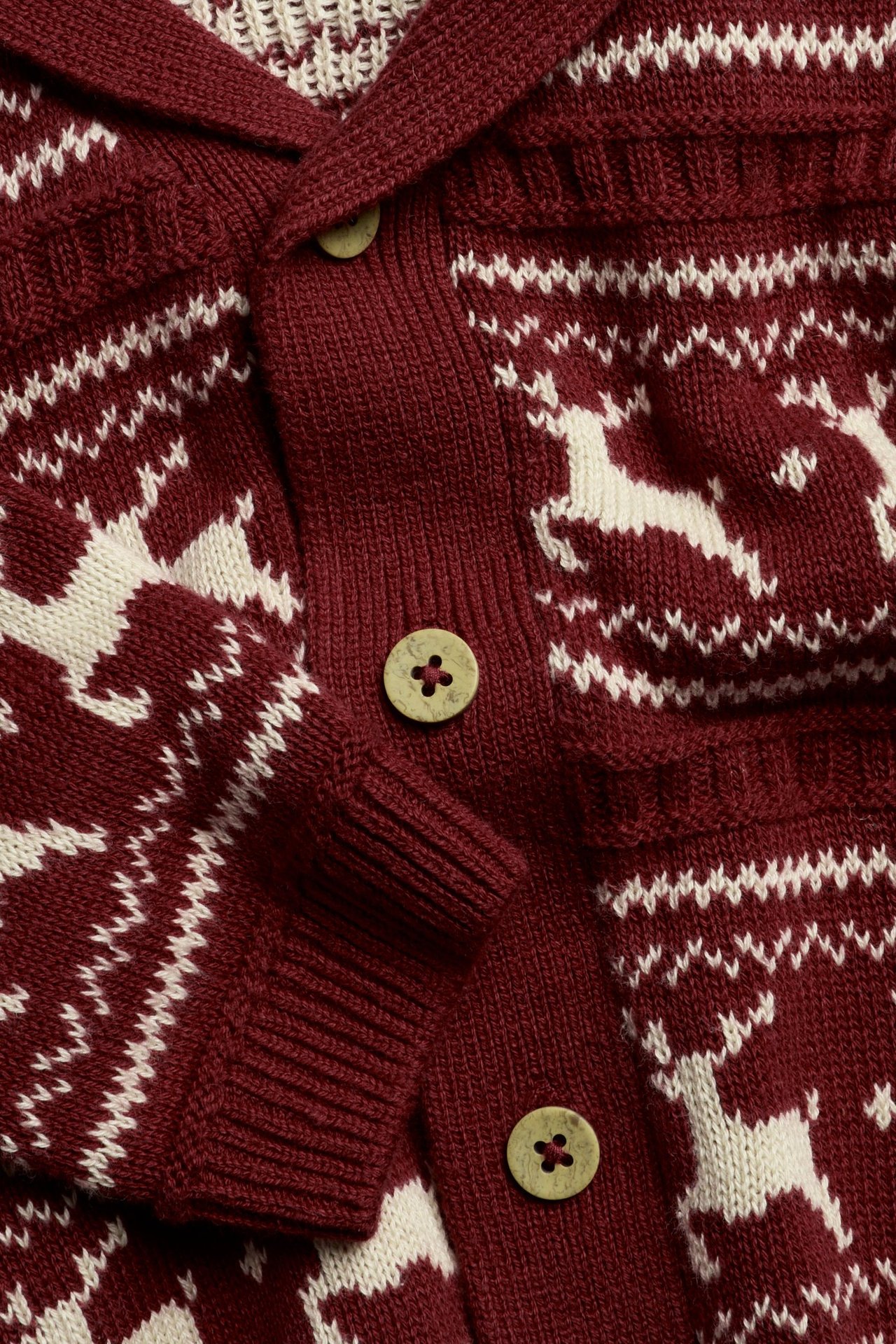 Lähikuva punaisesta jacquard-neulotusta puuvillaneuletakista, valkoisella porokuviolla, puunapeilla.
