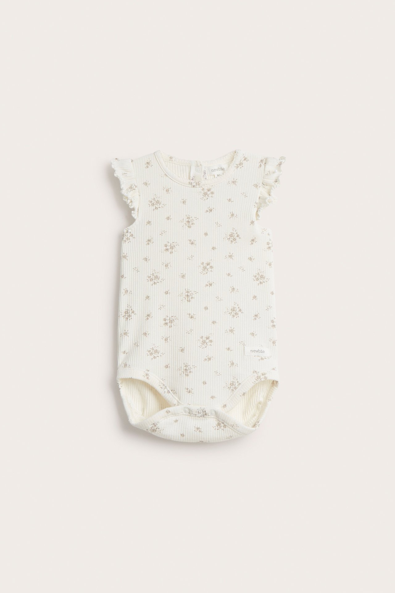 Frontvy av en offwhite ribbad babybody med blommigt mönster och volangärmar.