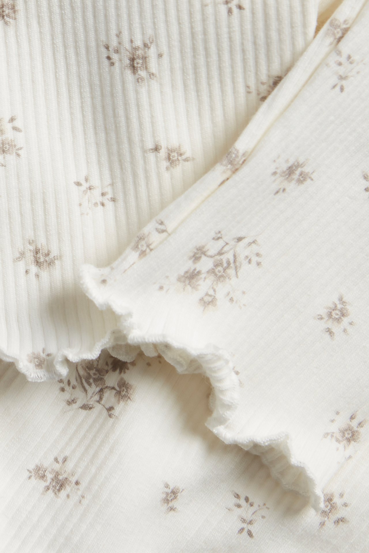 Närbild av offwhite ribbade leggings med brunt blommönster och en fin baby lock-kant.