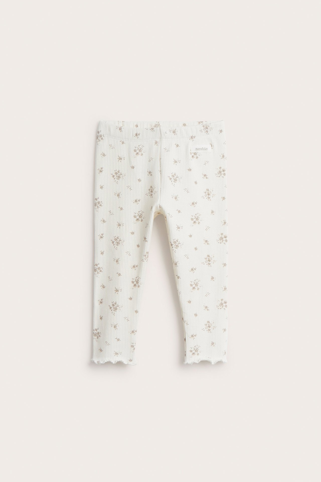 Frontvy av offwhite ribbade baby leggings med litet blommönster och baby lock-kanter.