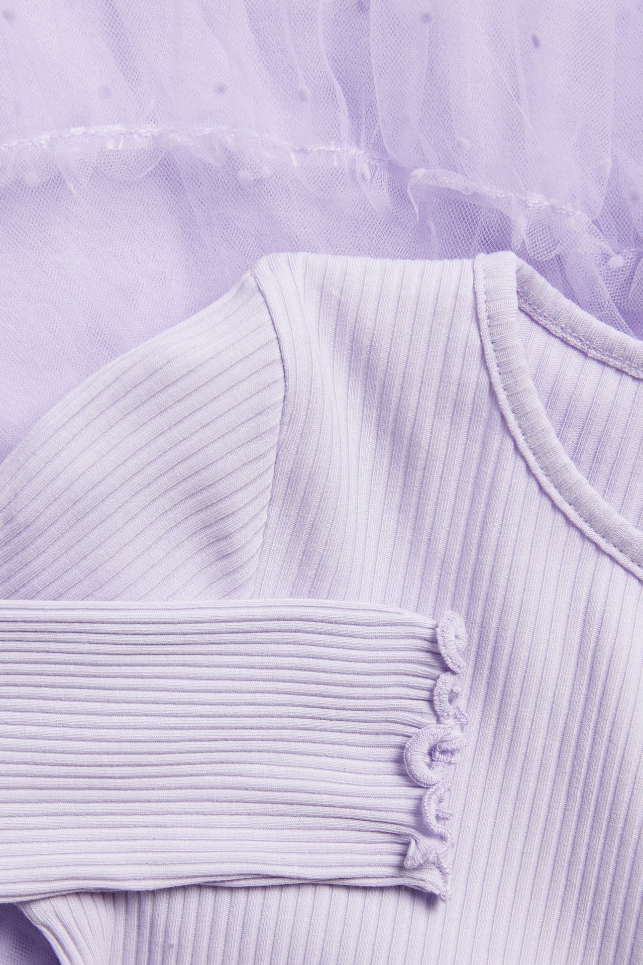 Zbliżenie jasnofioletowej prążkowanej sukienki z falbankowym mankietem i tiulową spódnicą w kropki.