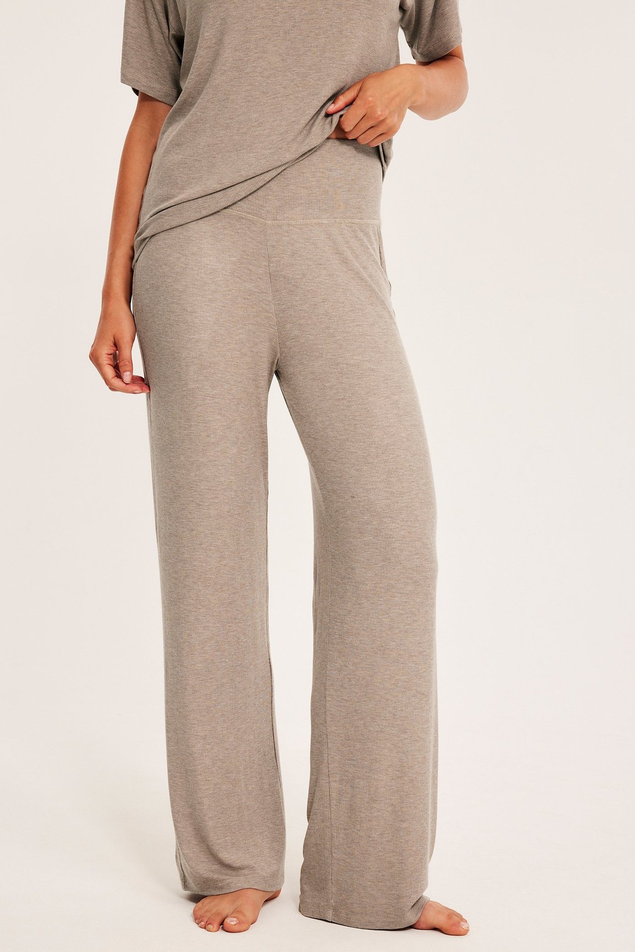 Naisen etukuva beigenmelange leveälahkeisissa viskoosipyjamahousuissa ja lyhythihaisessa paidassa.