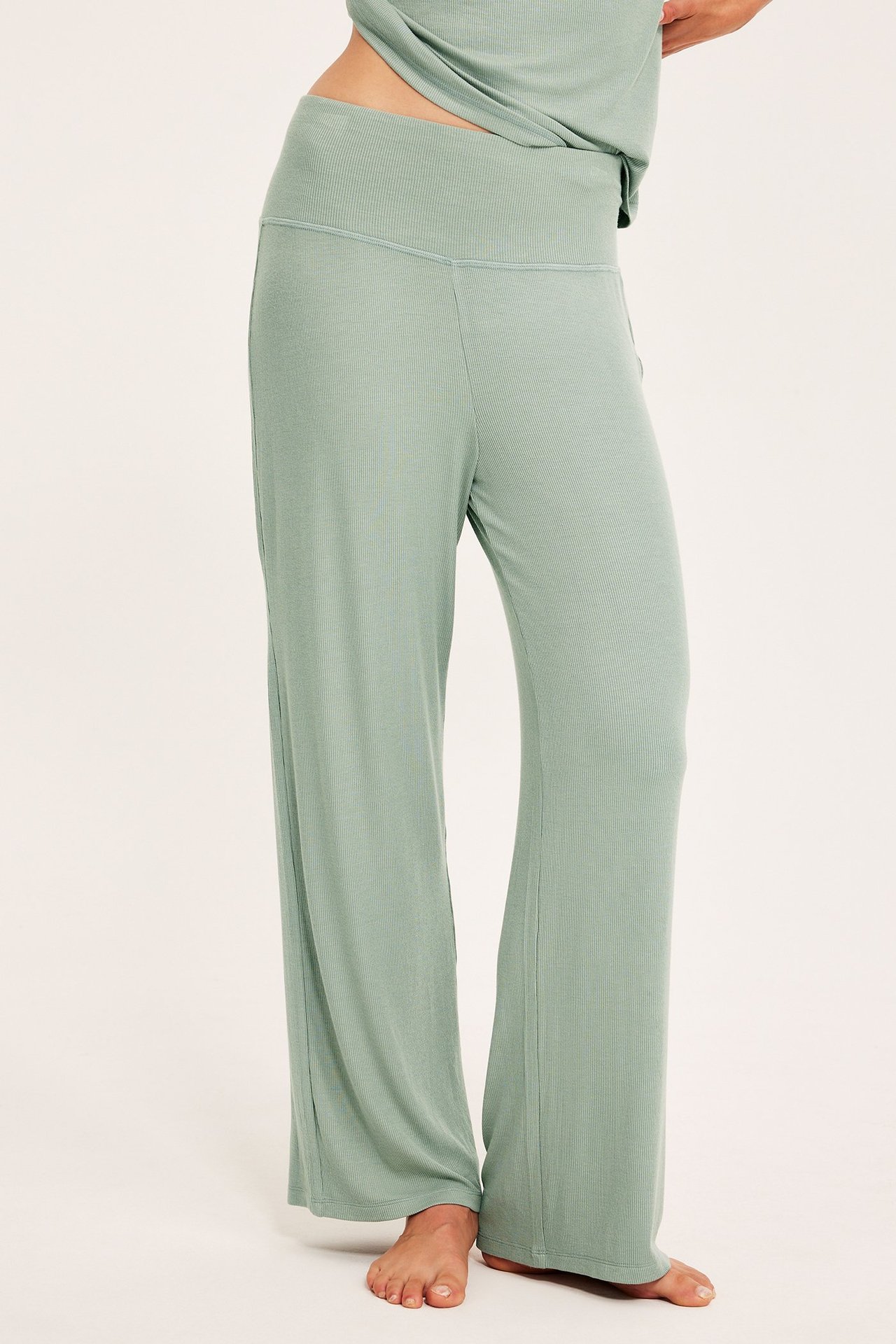 Naisen sivukuva: vaaleanvihreät leveälahkeiset pyjamahousut ja leveä ribbivyötärö.