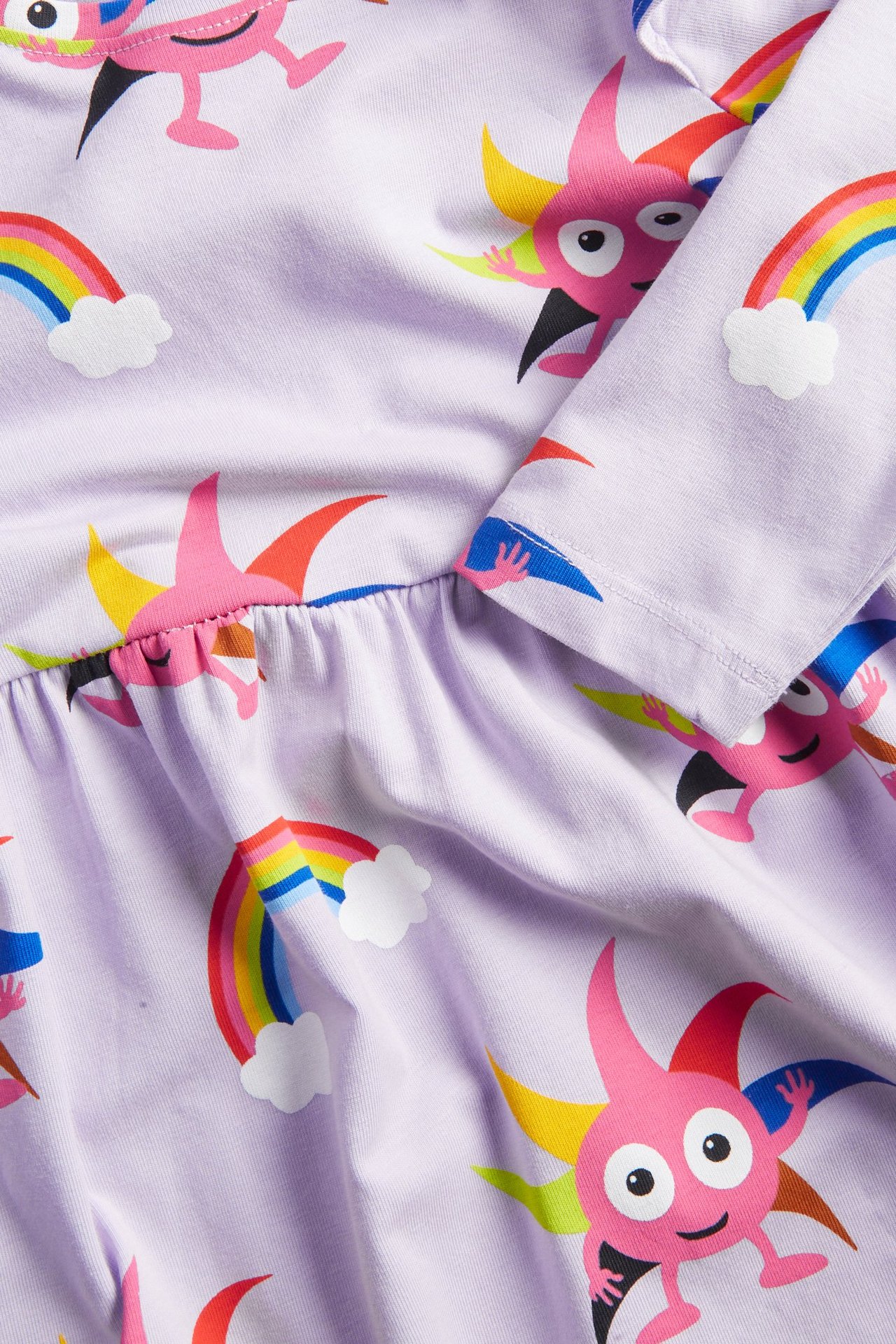 Zbliżenie na jasnofioletową sukienkę niemowlęcą z dżerseju z kolorowym wzorem Babblarna i tęczy.