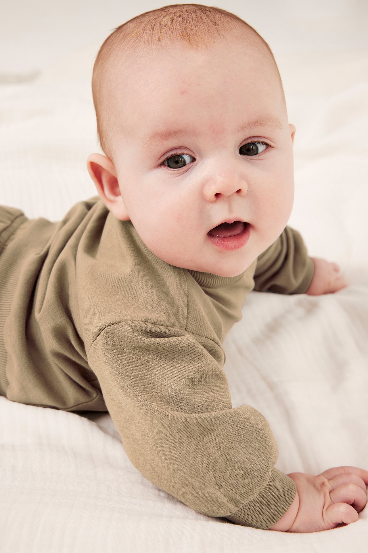 Frontvy av en baby i en ljusbrun långärmad sweatshirt med ribbade muddar.
