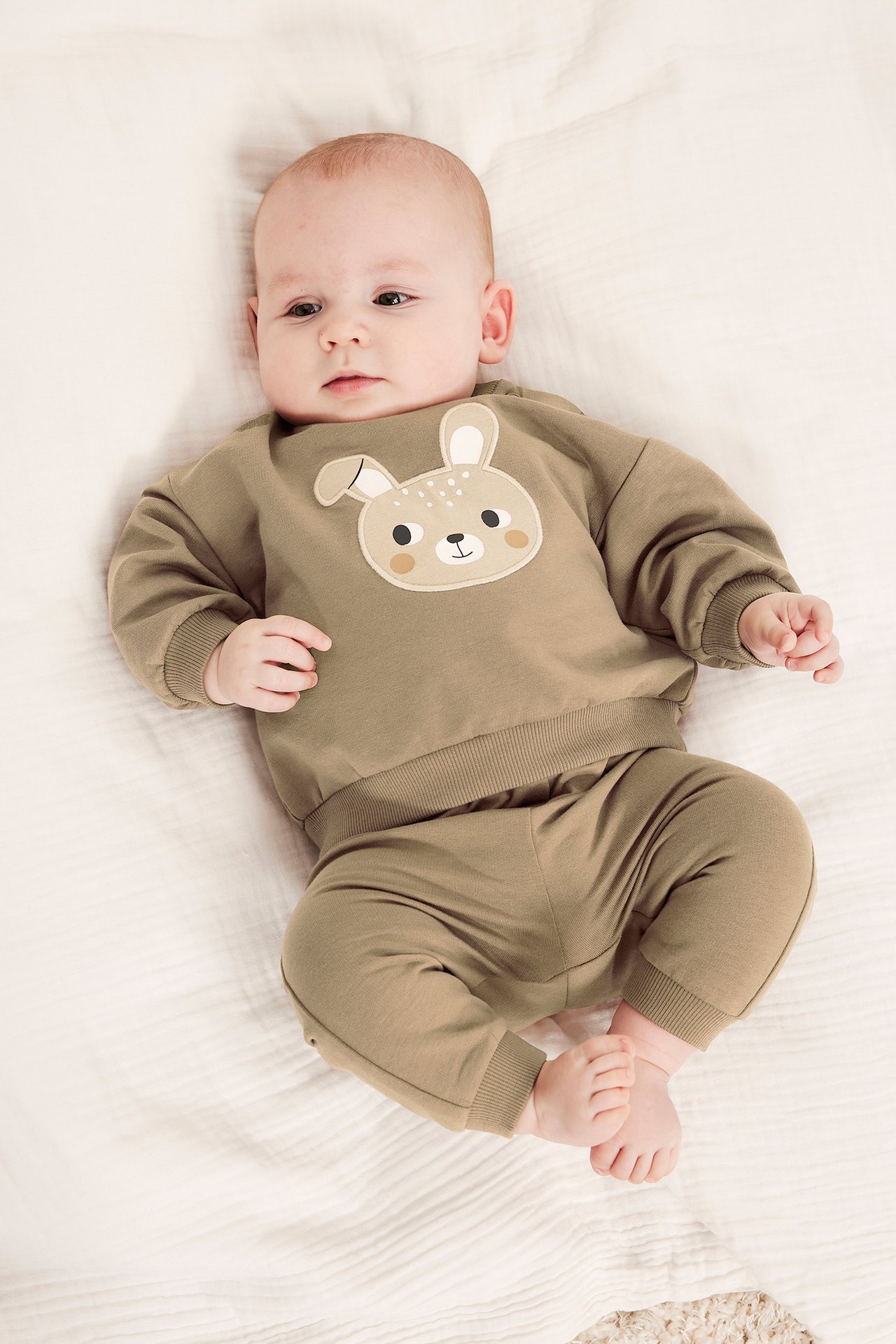 Framifrån, baby i brun bomullssweatshirt med kaninapplikation och matchande byxor.