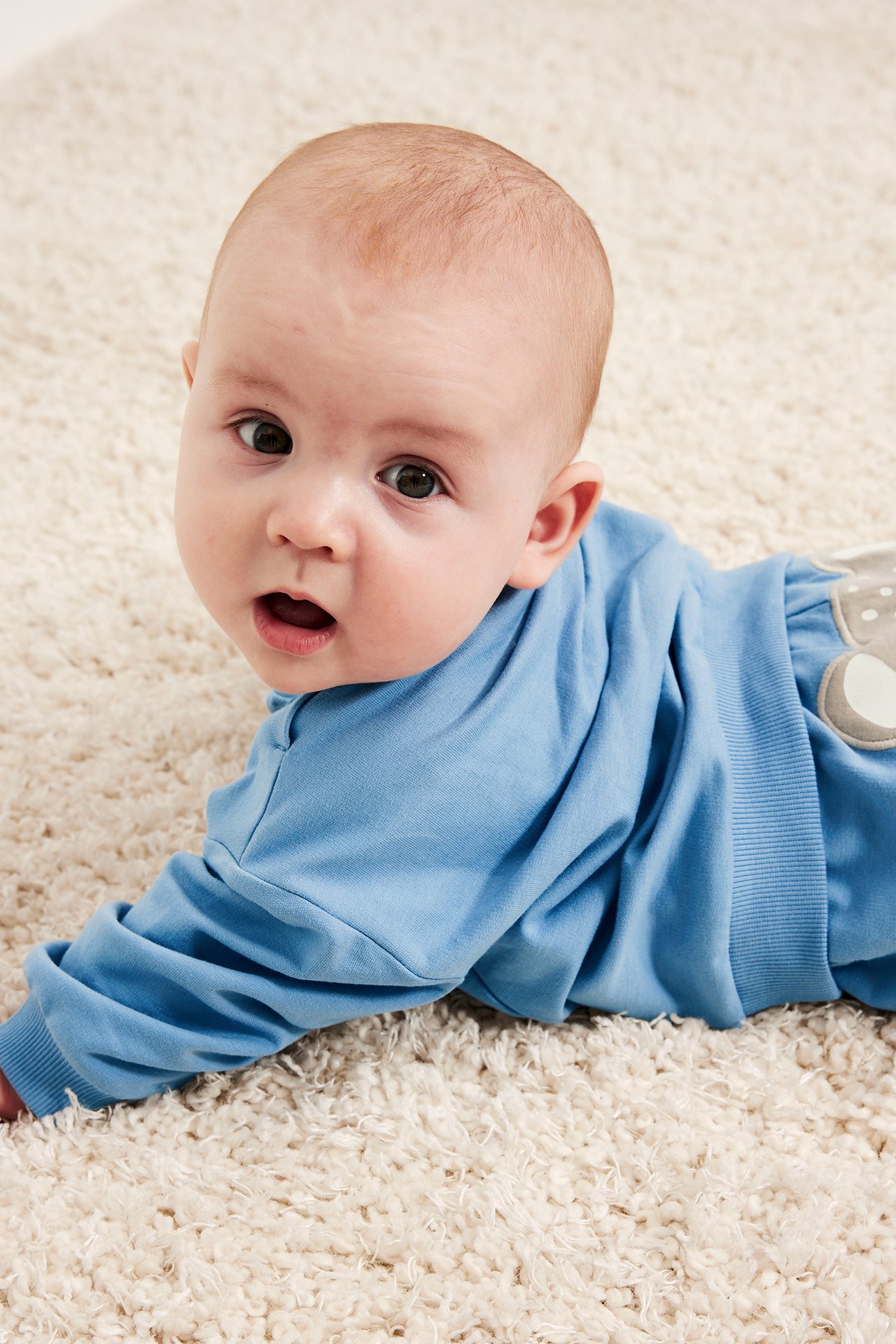Närbild på en baby i en blå sweatshirt med applikation, matchad med gråprickiga byxor.