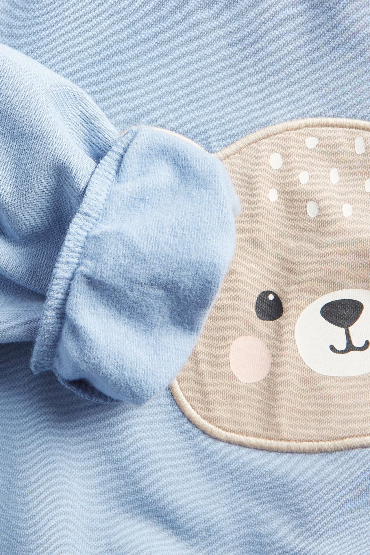 Zbliżenie na jasnoniebieską bluzę niemowlęcą z beżową aplikacją misia z przodu.