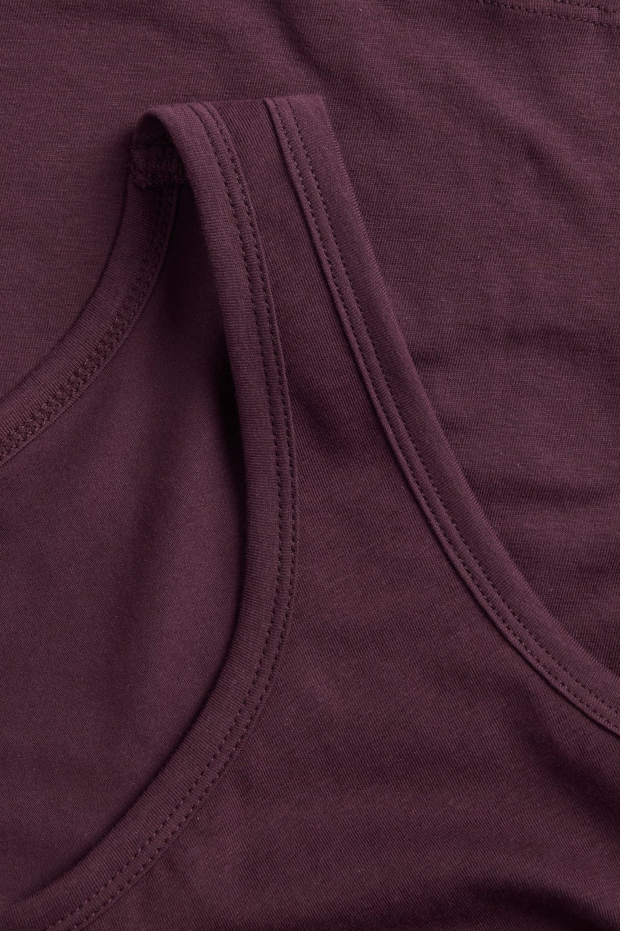 Zbliżenie na ciemnoczerwony top na ramiączkach z widocznymi szwami przy dekolcie i ramiączku.