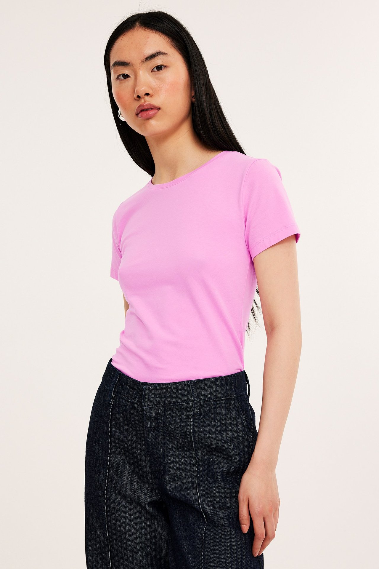 Forfra: kvinne i en figurnær rosa kortermet basetopp og mørkeblå vide bukser.