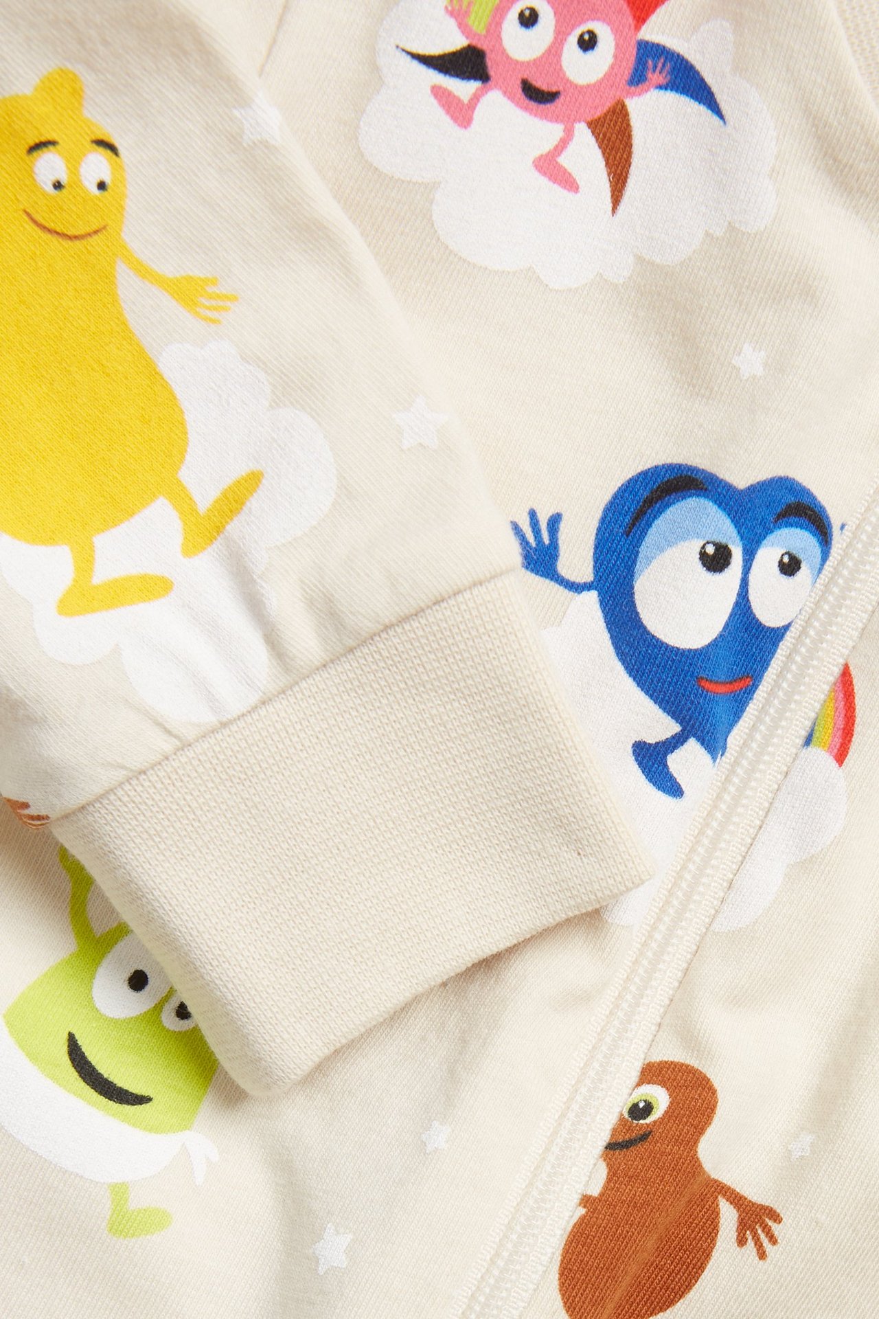 Zbliżenie na jasnobeżowy pajacyk niemowlęcy z kolorowym nadrukiem Babblarna i zamkiem błyskawicznym z przodu.