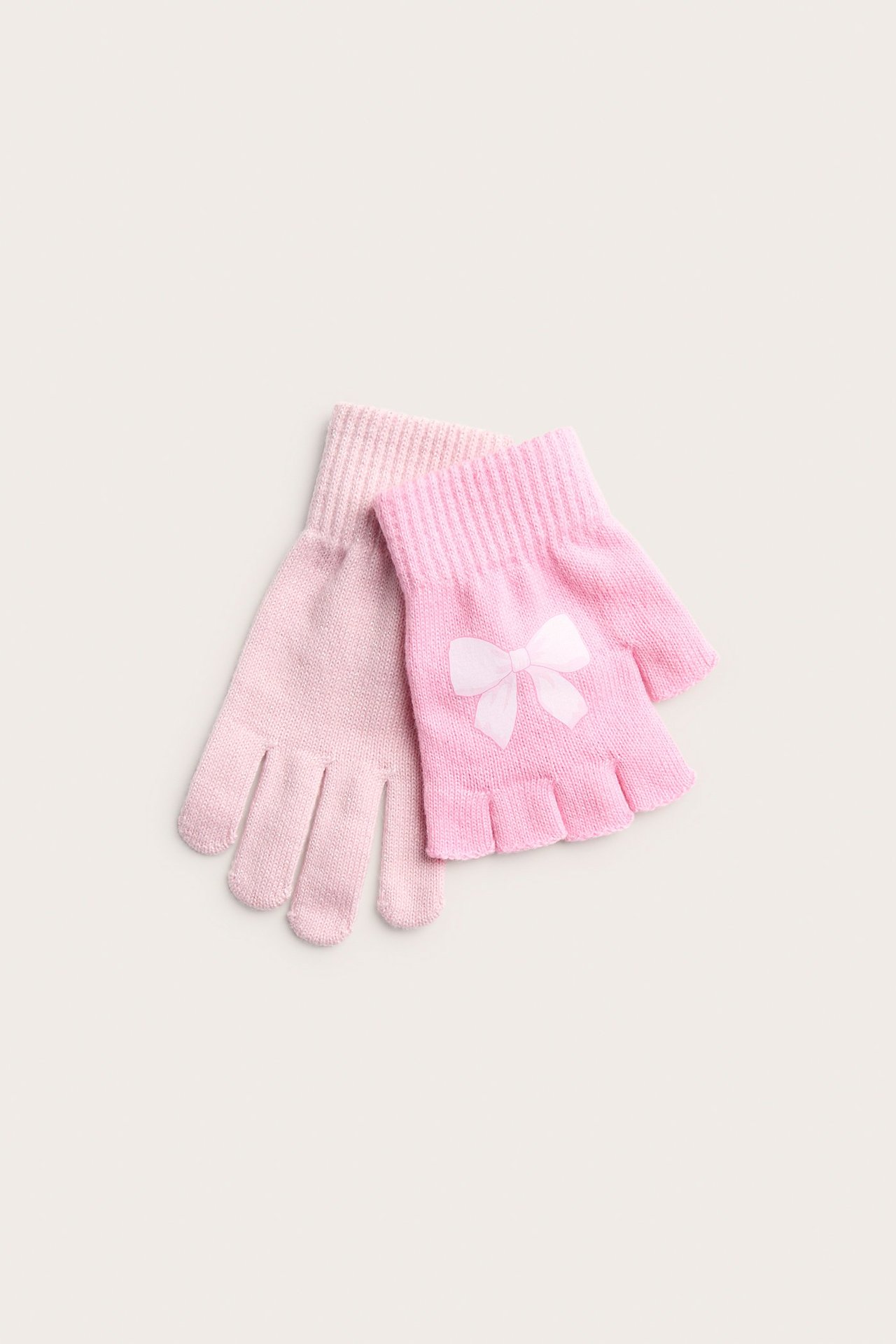 Widok z góry na dwie różowe dzianinowe rękawiczki dziecięce bez palców, jedna z białym nadrukiem kokardki.