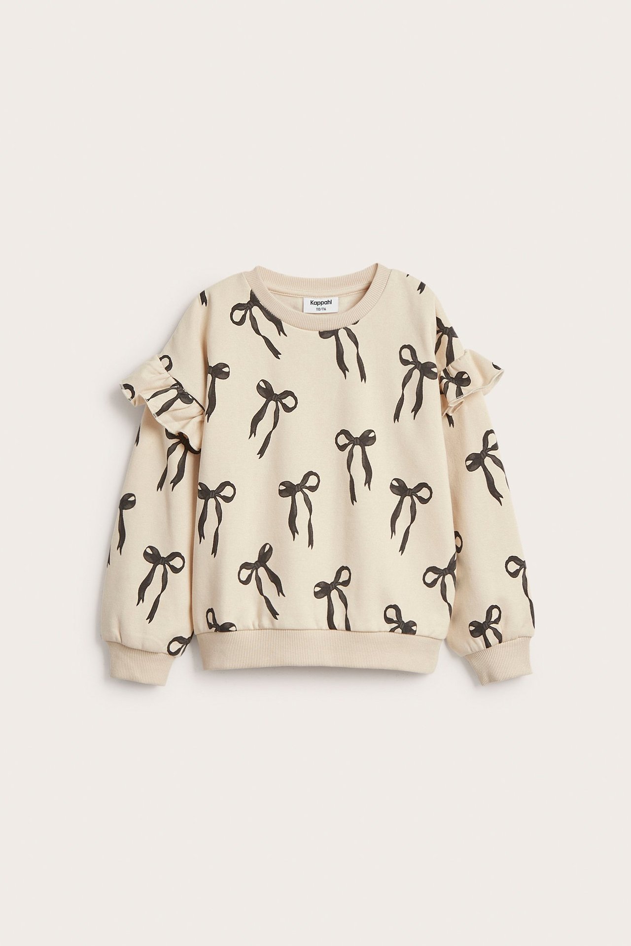 Widok z przodu: beżowa bluza dziecięca z czarnym wzorem kokardek i falbankami na rękawach.